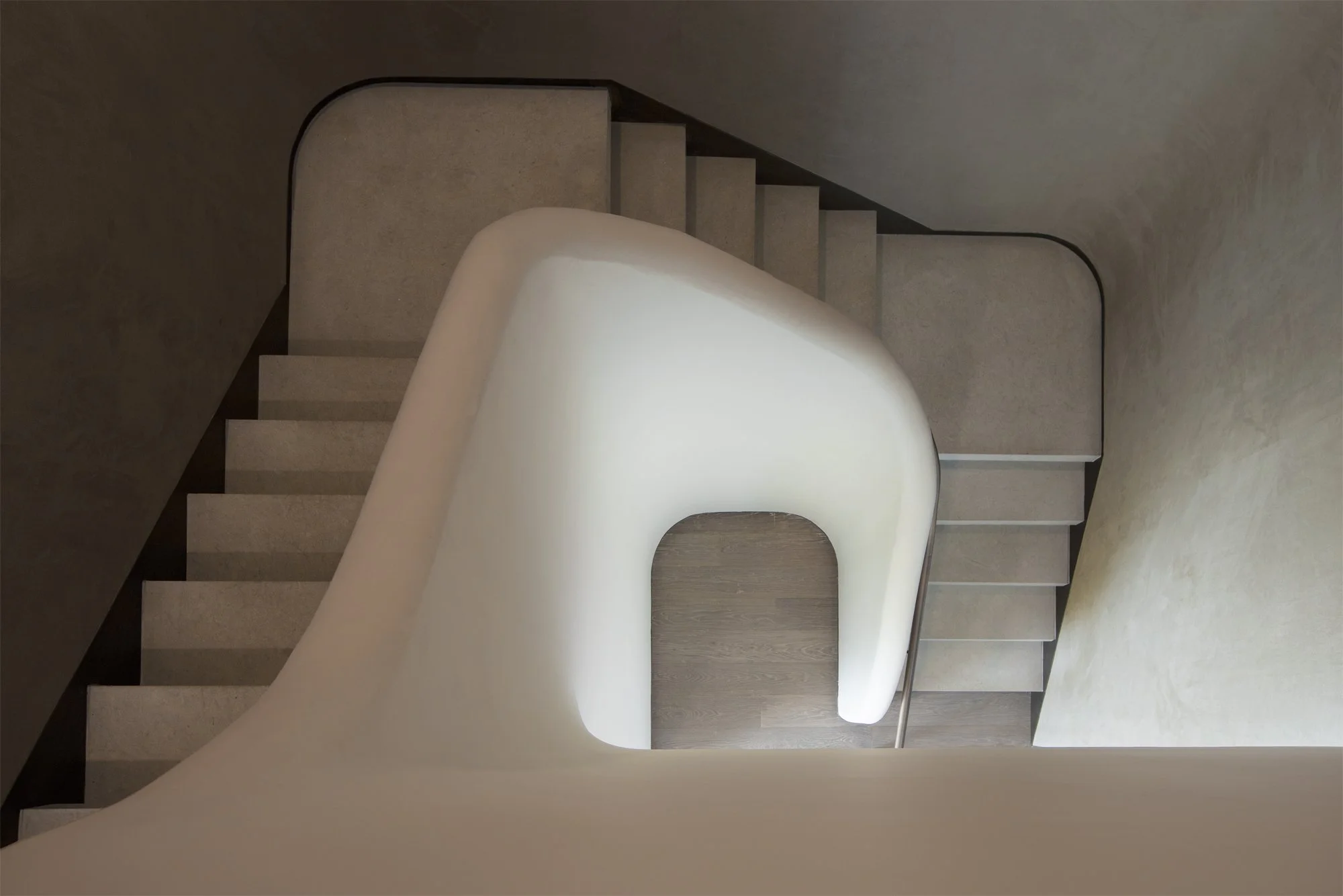 JGNA residential sculptural plaster stair viewed from above, with curved walls and stone treads