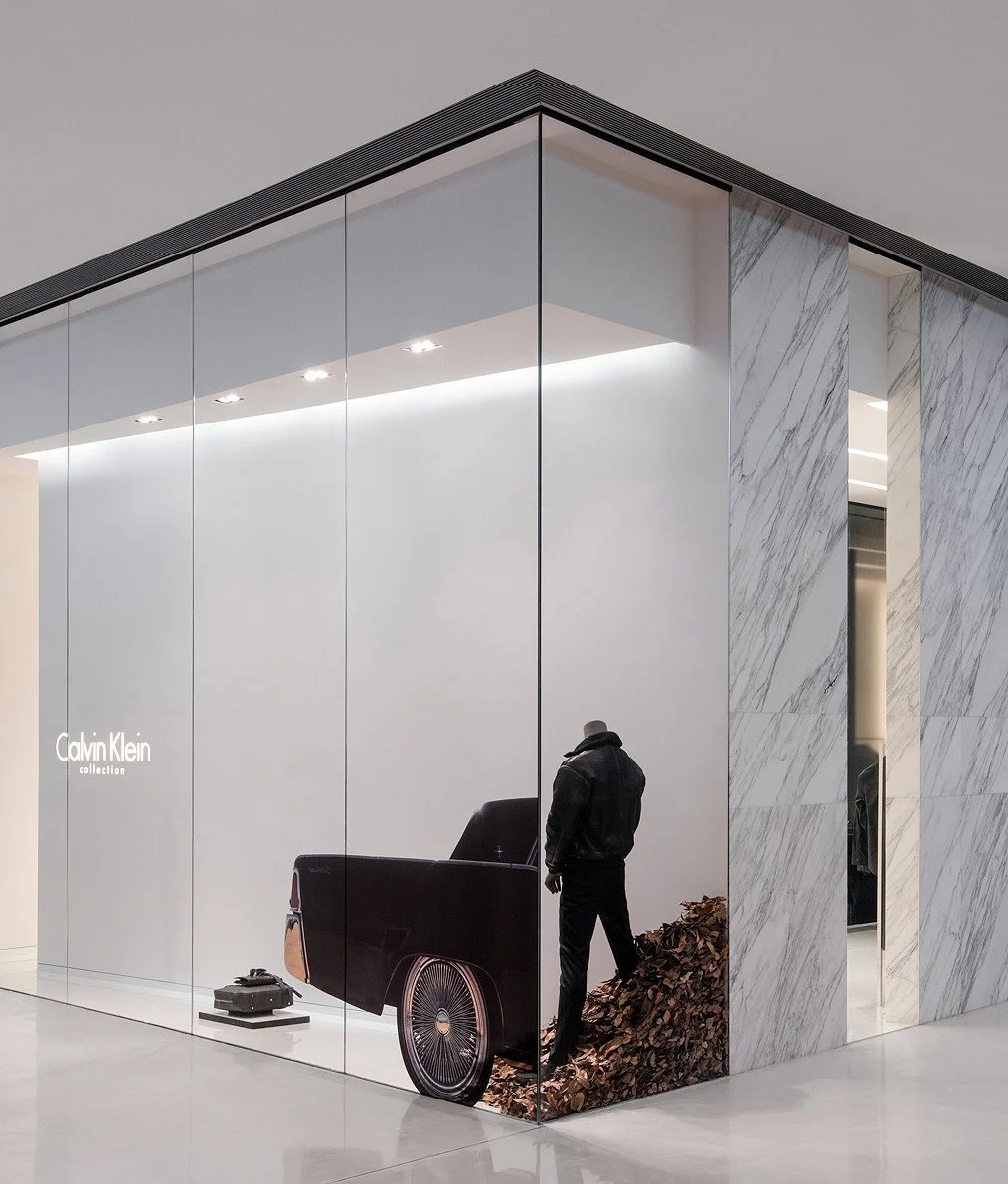Calvin Klein Collection window display with a sculptural vehicle installation behind a marble-framed glass corner