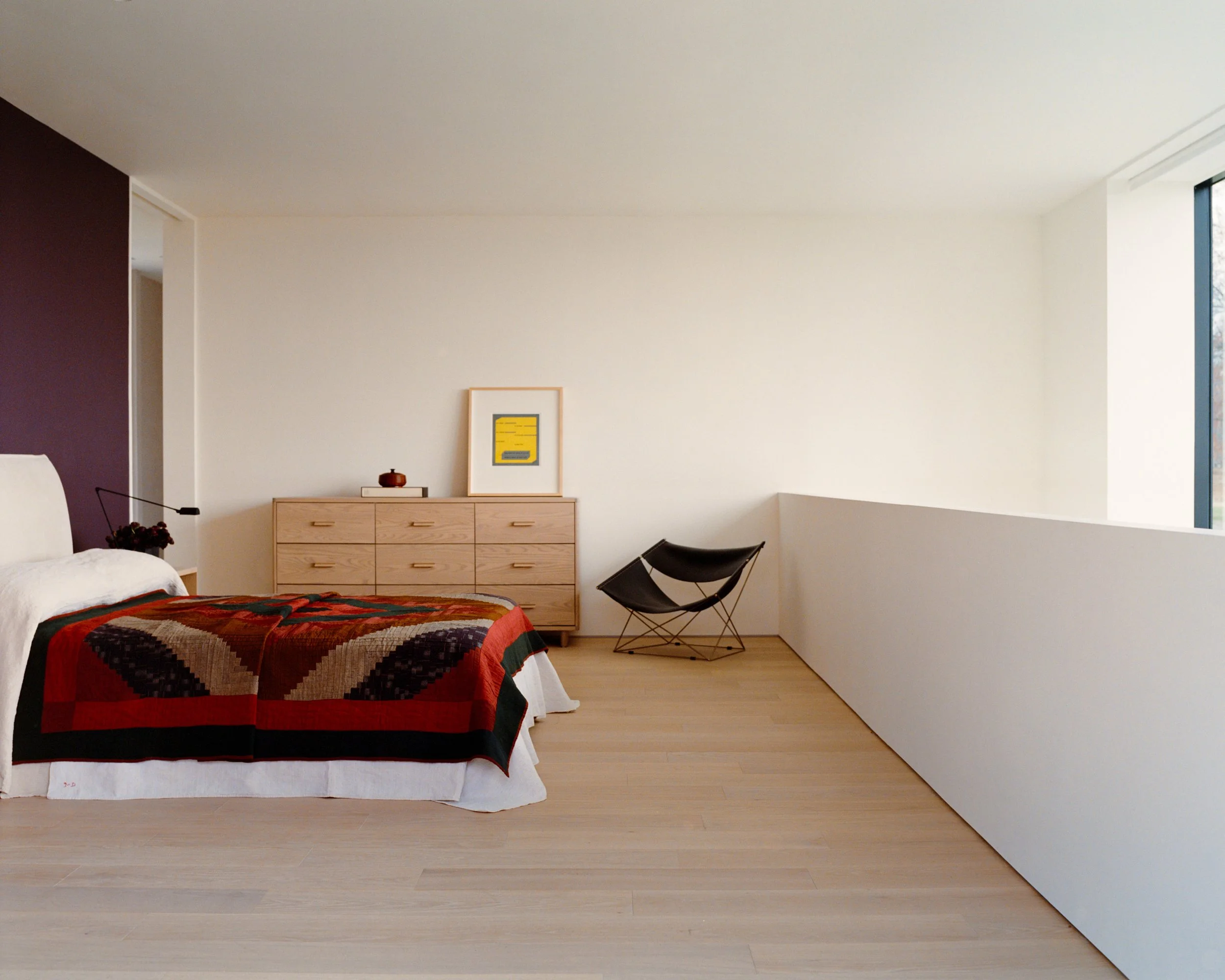 Bedroom with a plum accent wall, oak dresser, and a patchwork quilt at a Ghent, NY home by JG Neukomm Architecture