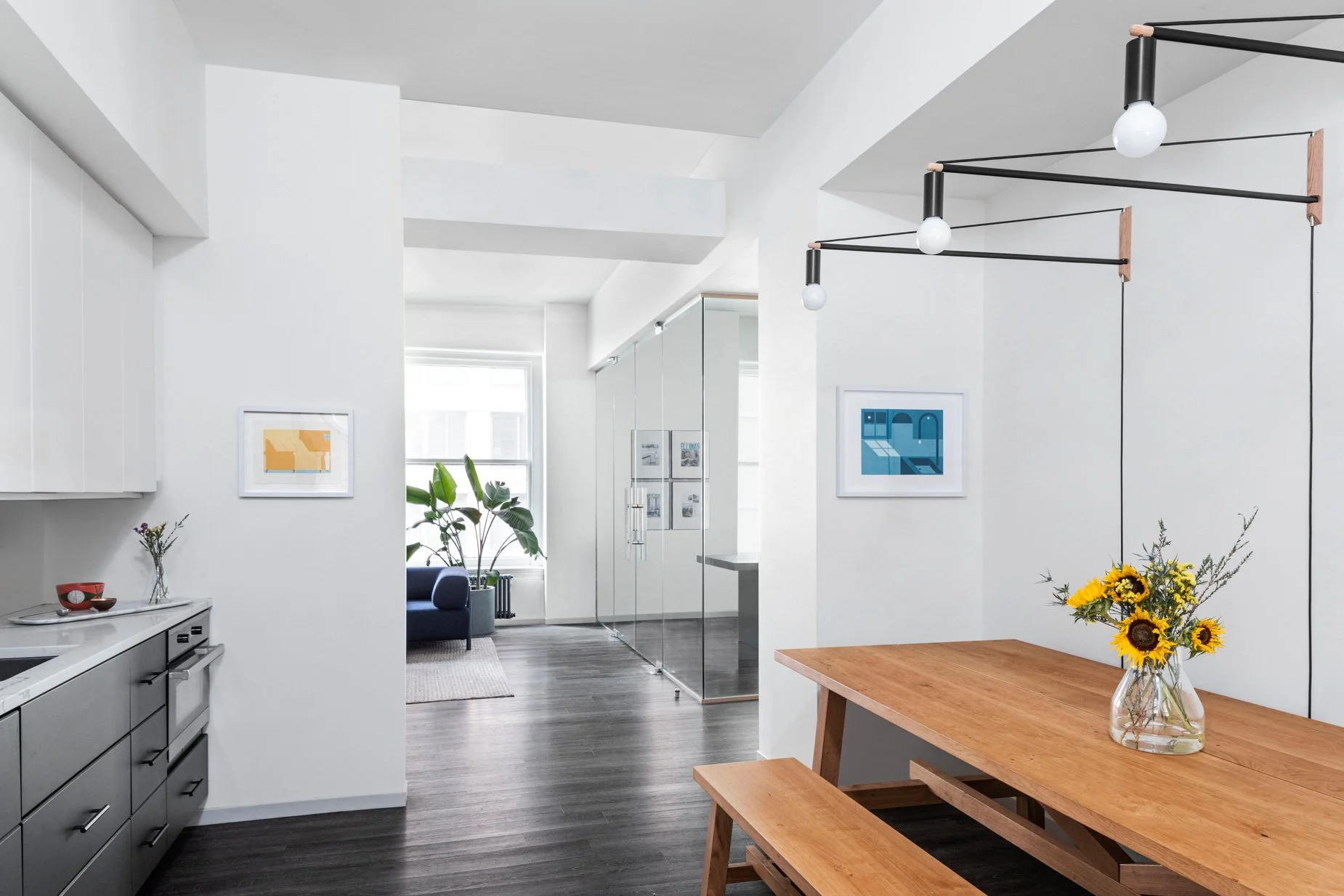 JGNA studio kitchen and dining area with an oak table, sculptural linear pendant lighting, and framed prints