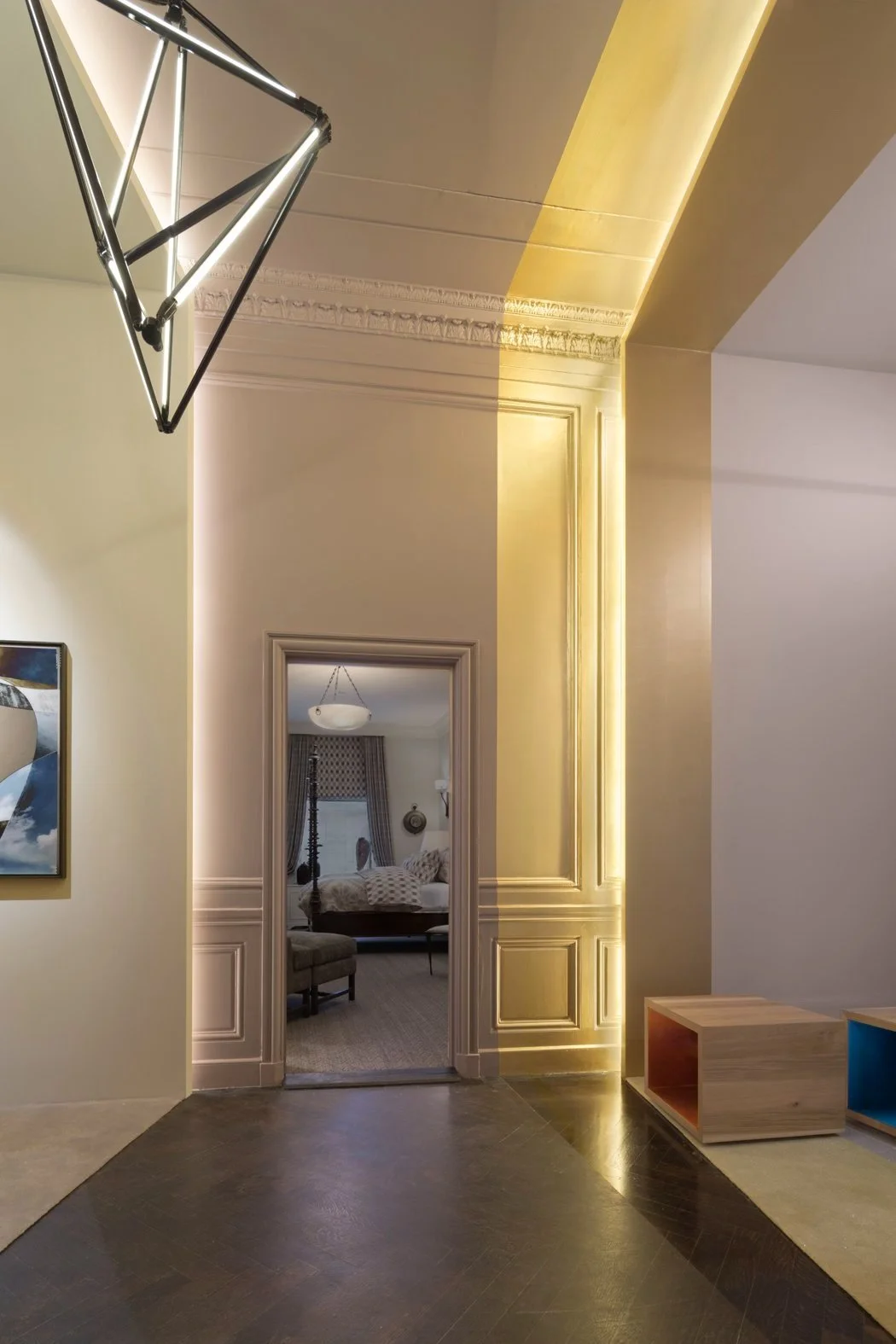 JGNA corridor looking toward a bedroom threshold, with a faceted pendant and warm cove lighting along the molding