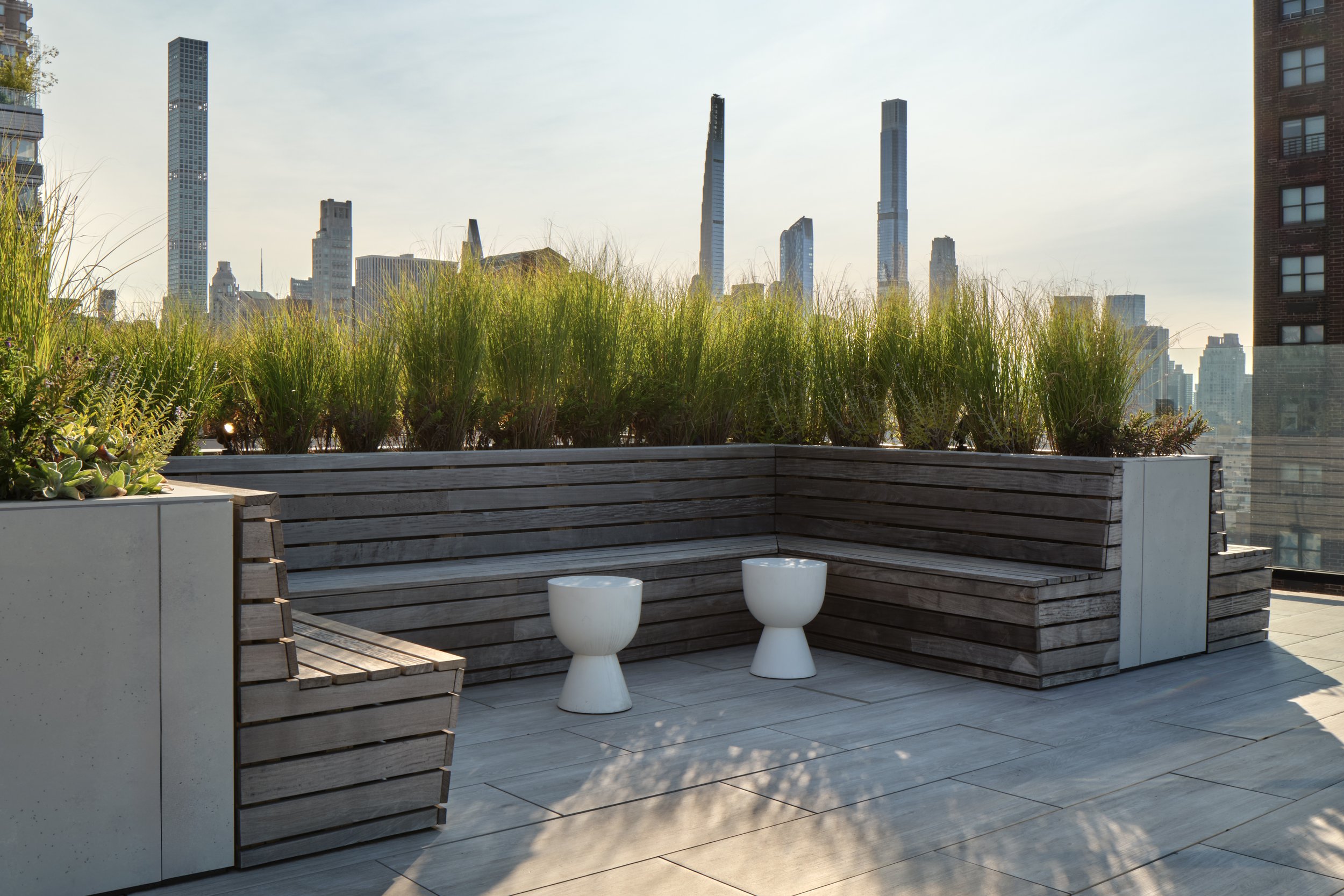 JGNA residential rooftop terrace with a built-in timber bench, ornamental grasses, and a Manhattan skyline view