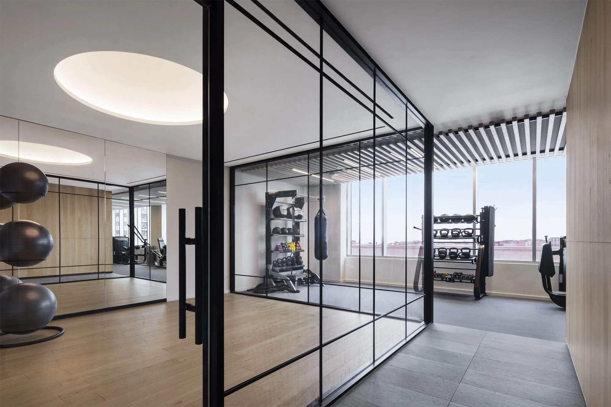JGNA residential fitness center with a mirrored studio, steel-framed glass partition, and equipment by the windows