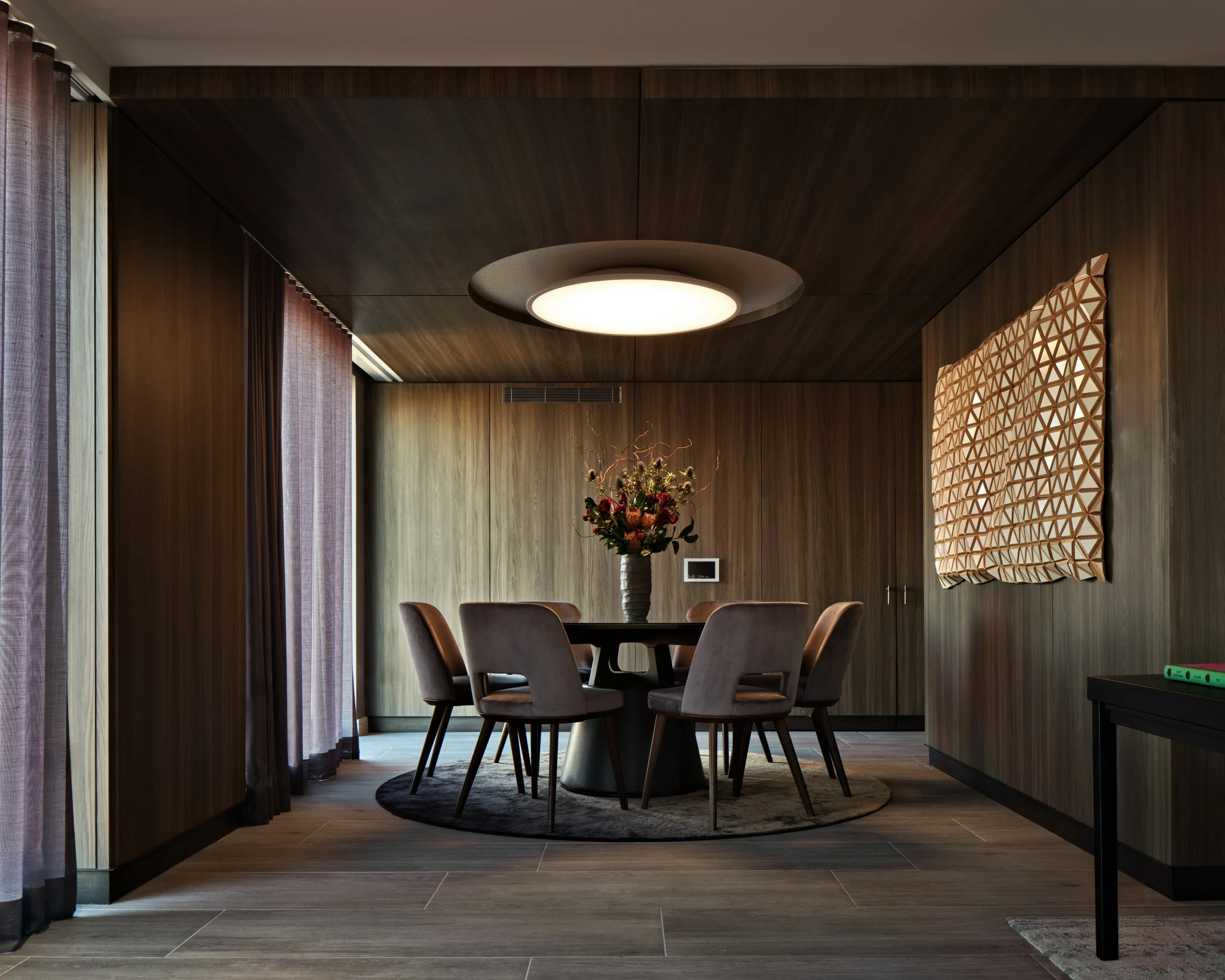 JGNA residential dining nook with a round table, leather chairs, walnut paneling, and a disc pendant light