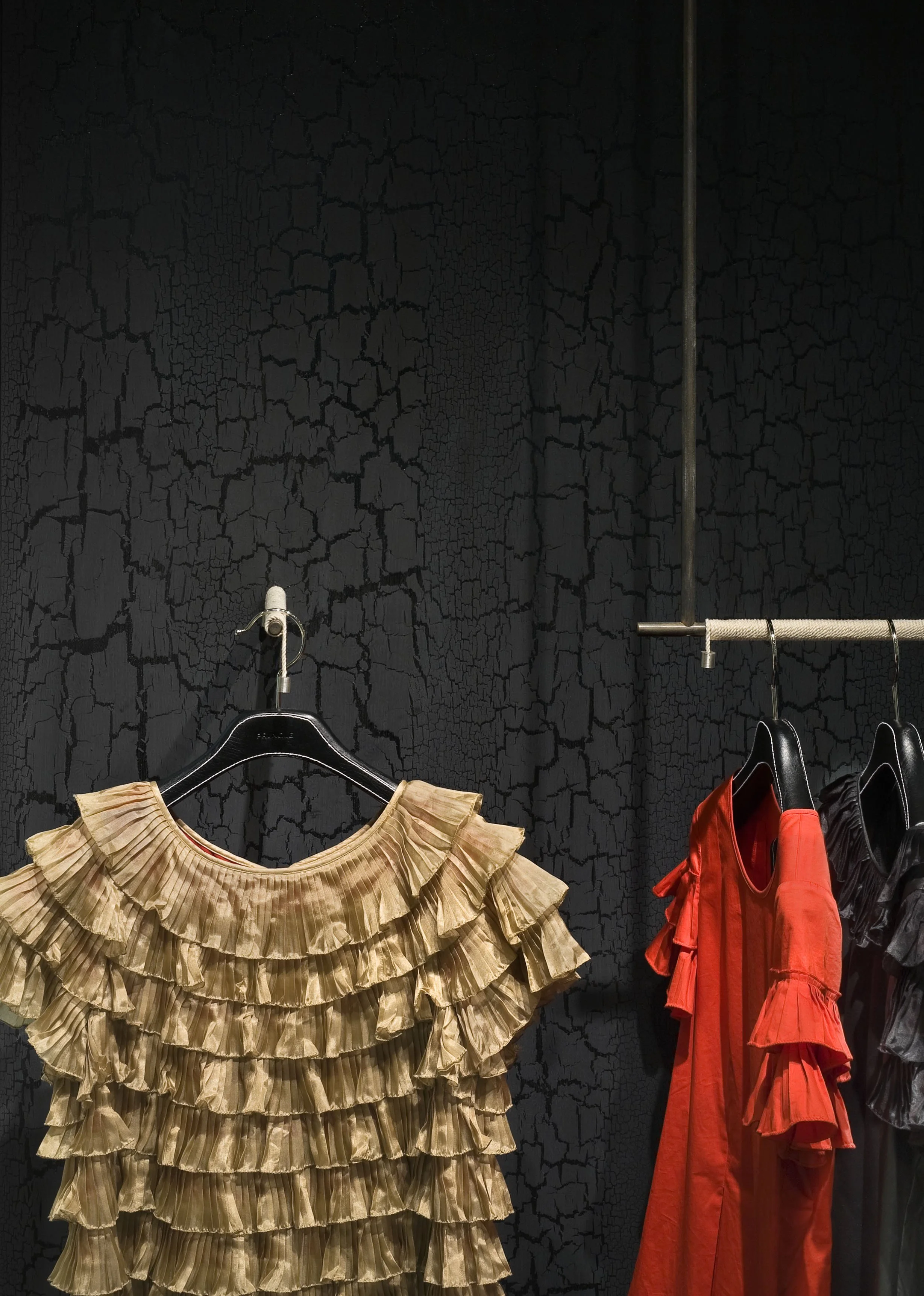 JGNA boutique detail with a gold ruffled top and red dress on hangers against a crackled black textured wall