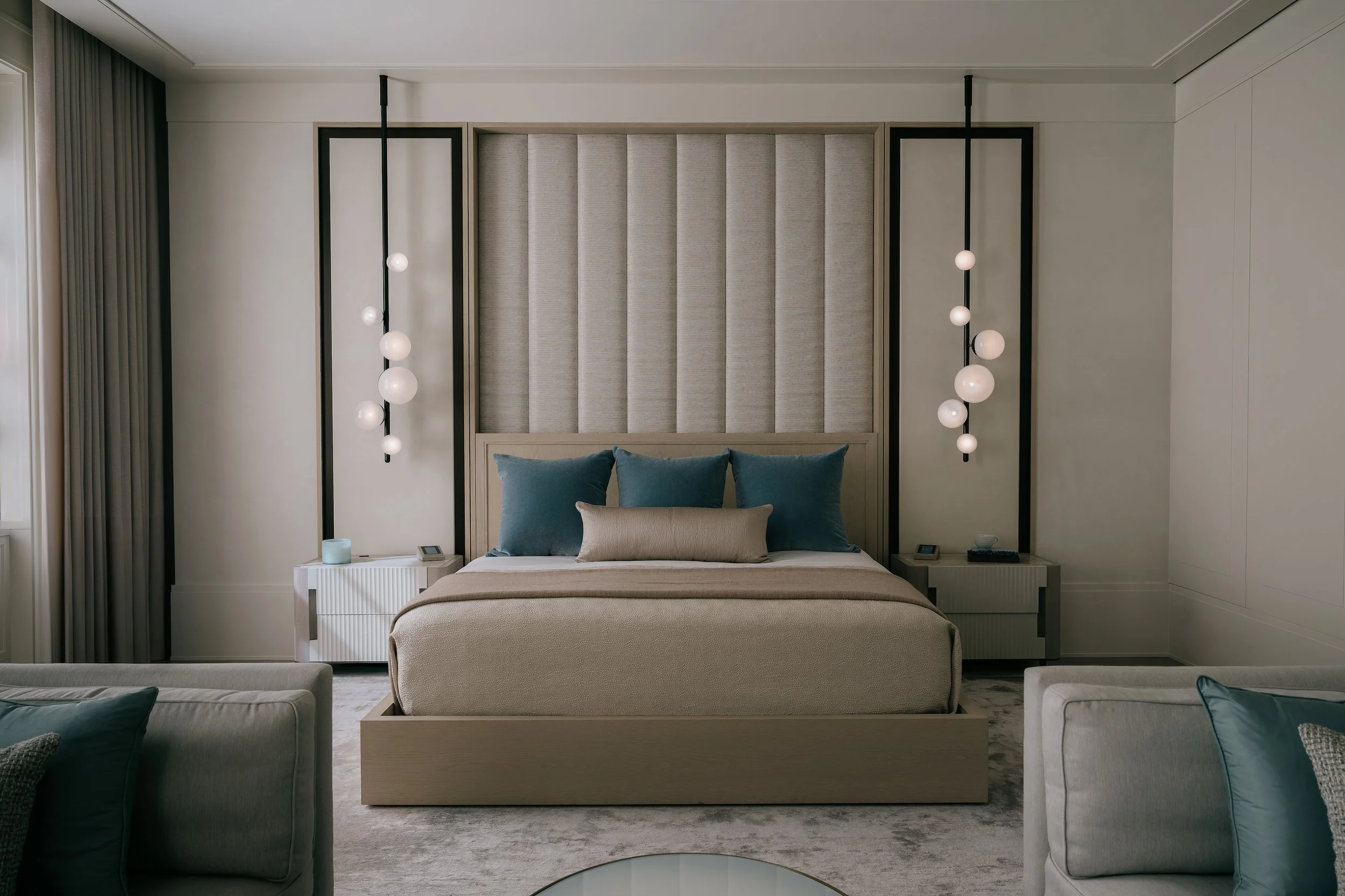 Primary bedroom with a tall channel-tufted headboard wall and cascading glass globe pendant lights
