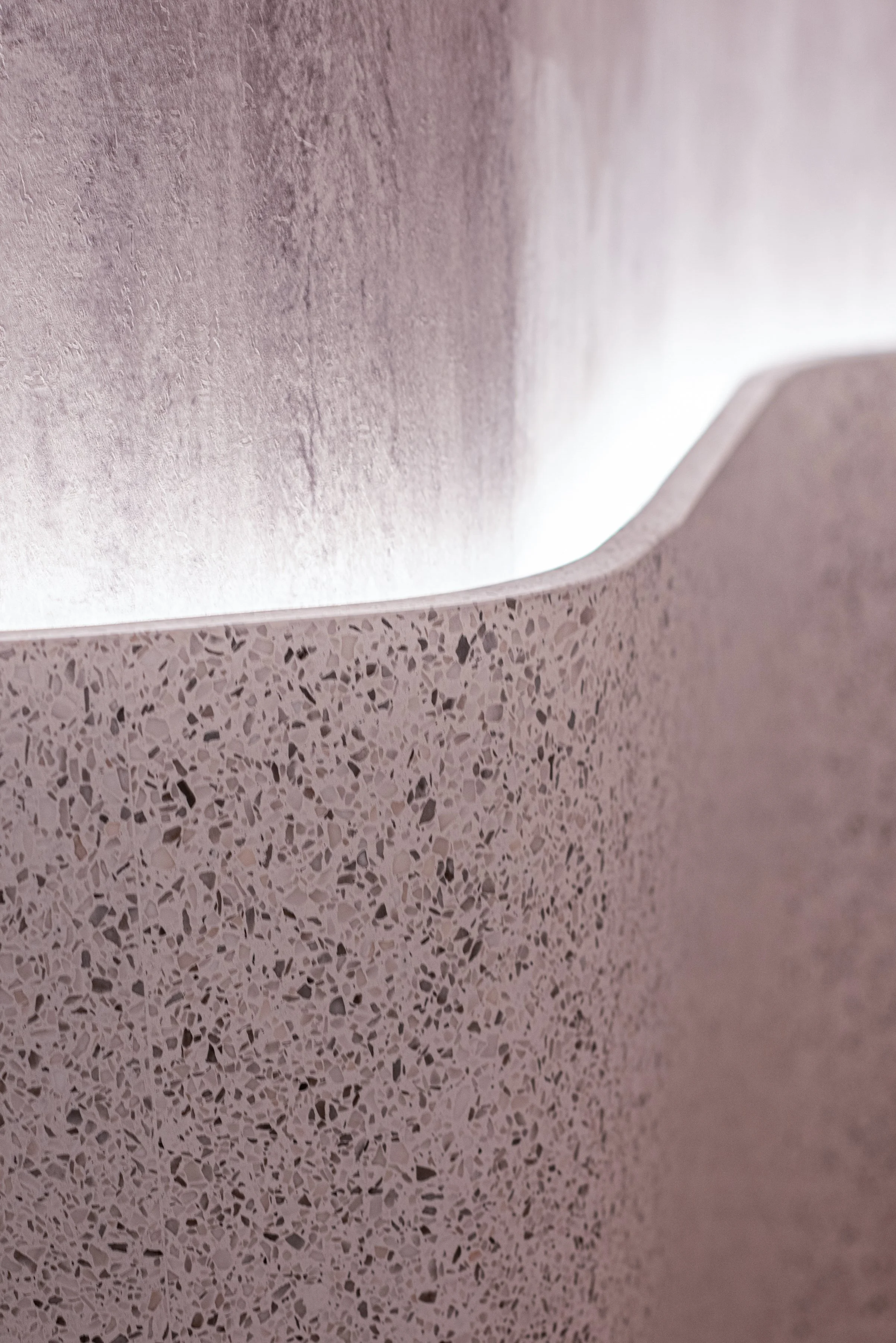 JGNA residential meditation room detail of a curved travertine wall meeting a pink terrazzo base with cove lighting