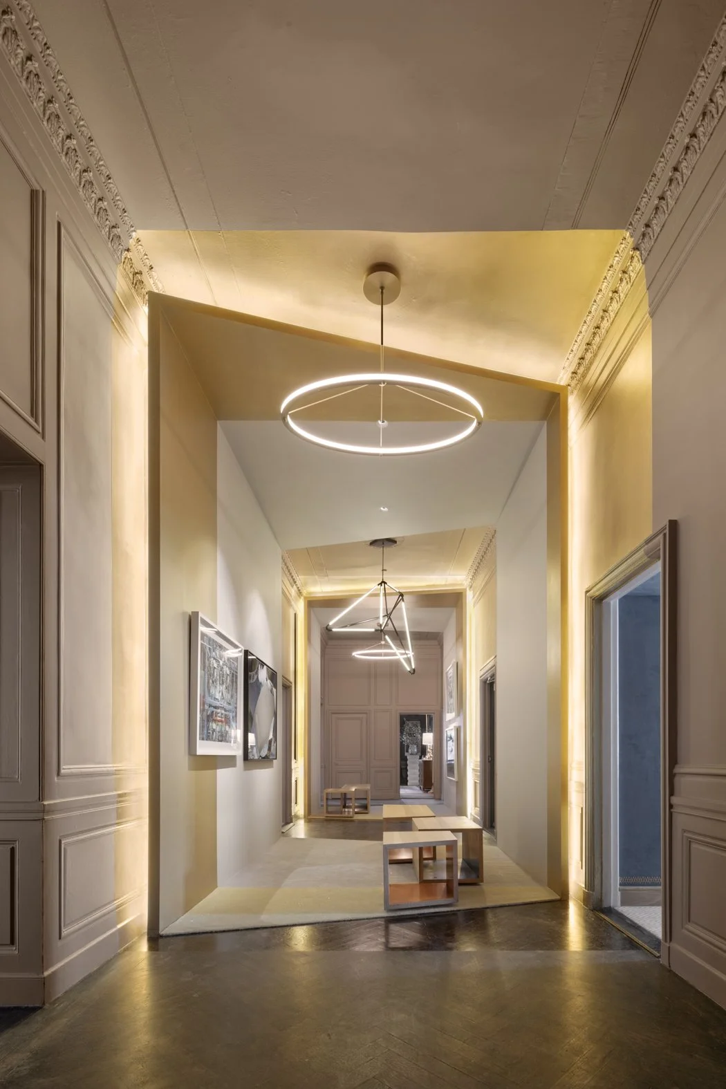 JGNA residence gallery hallway with a circular LED pendant, concealed cove lighting, and classic wall paneling
