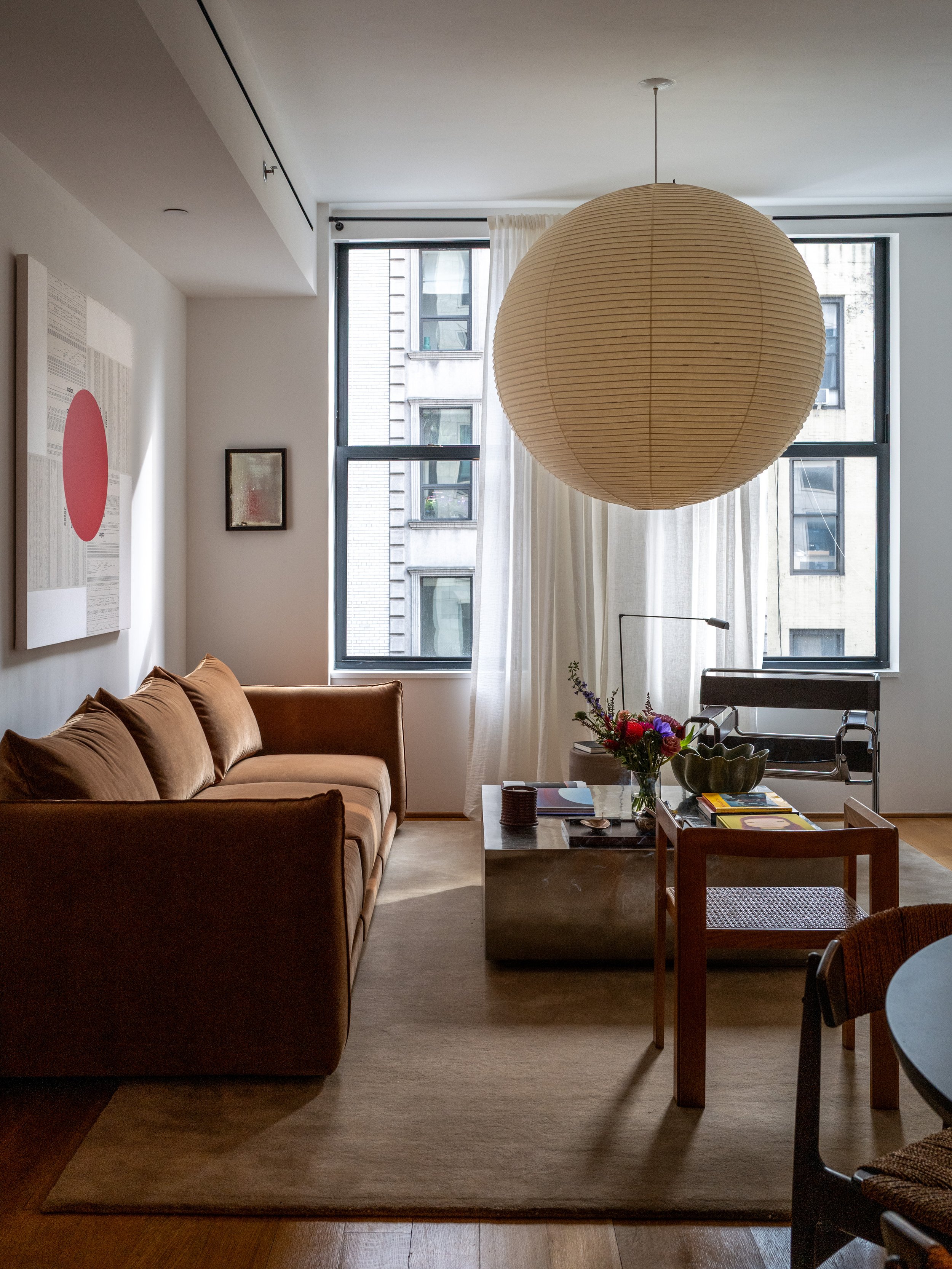 Wide view of open-plan living space with paper globe pendant, velvet sofa, and full-height windows