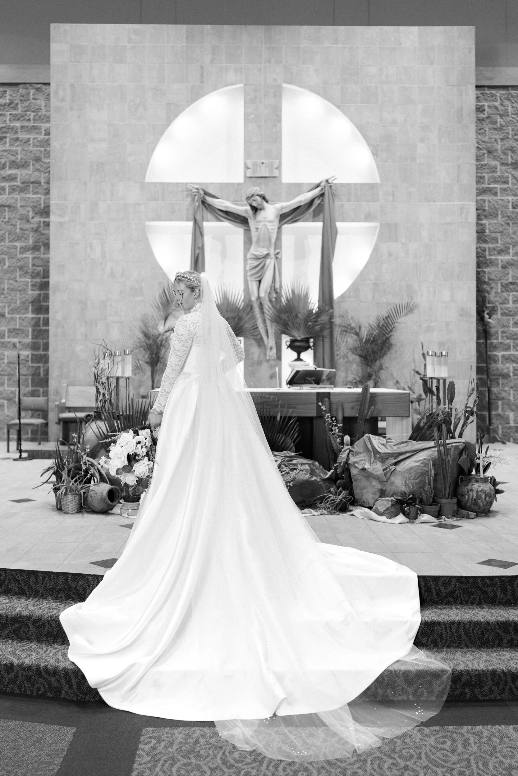 Bride looking down at her bouquet in her wedding gown with veil and crown in front of altar and crucifix for her bridal photos at St. Matthew Catholic Church
