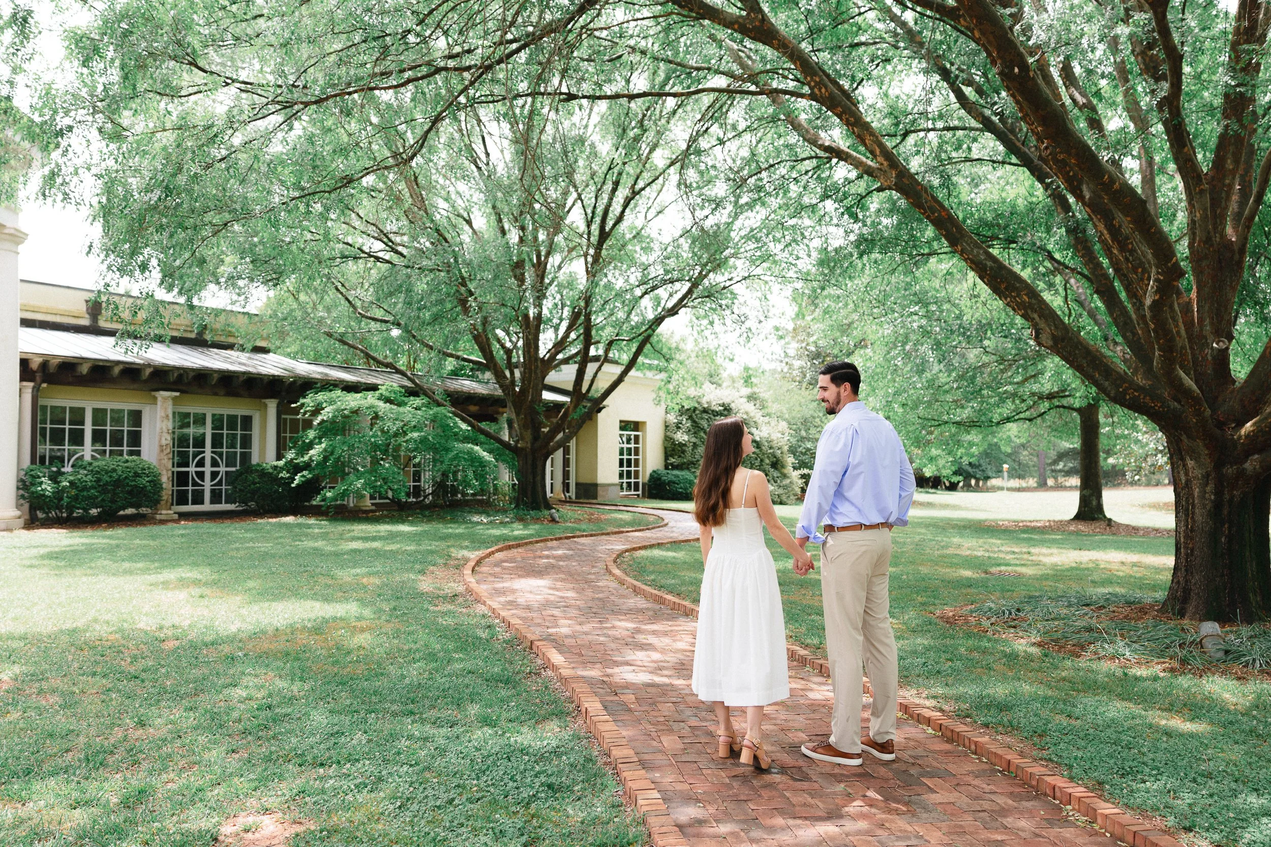 Engaged couple laughing and smiling at each other with Daniel Stowe Conservancy walking in tree covered park bright and airy by ParksPictures