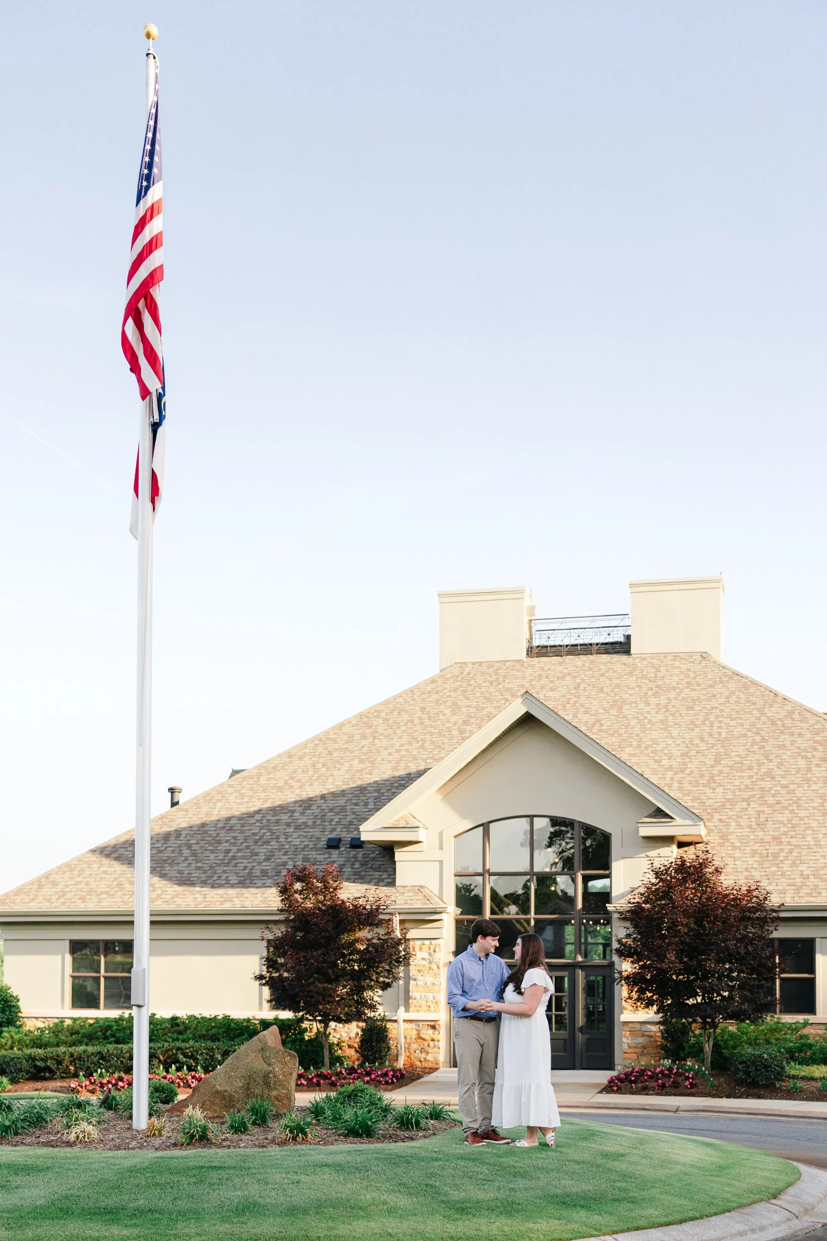 Engaged couple holding each other in front of clubhouse at NorthStone Country Club at sunset on film in a bright and airy aesthetic by ParksPictures