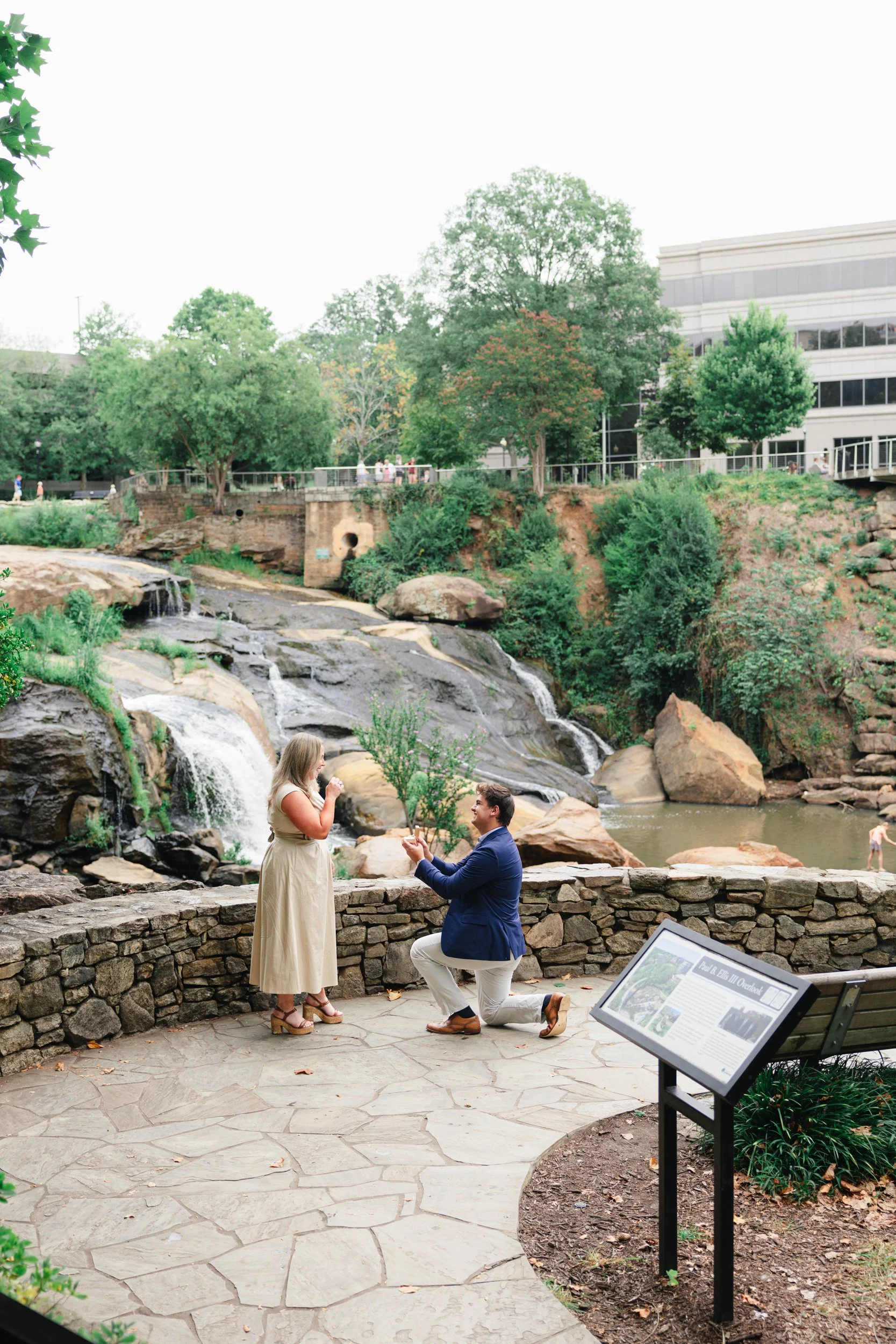 Boyfriend proposing on one knee to girlfriend in front of waterfall at Falls Park in Greenville SC, by ParksPictures