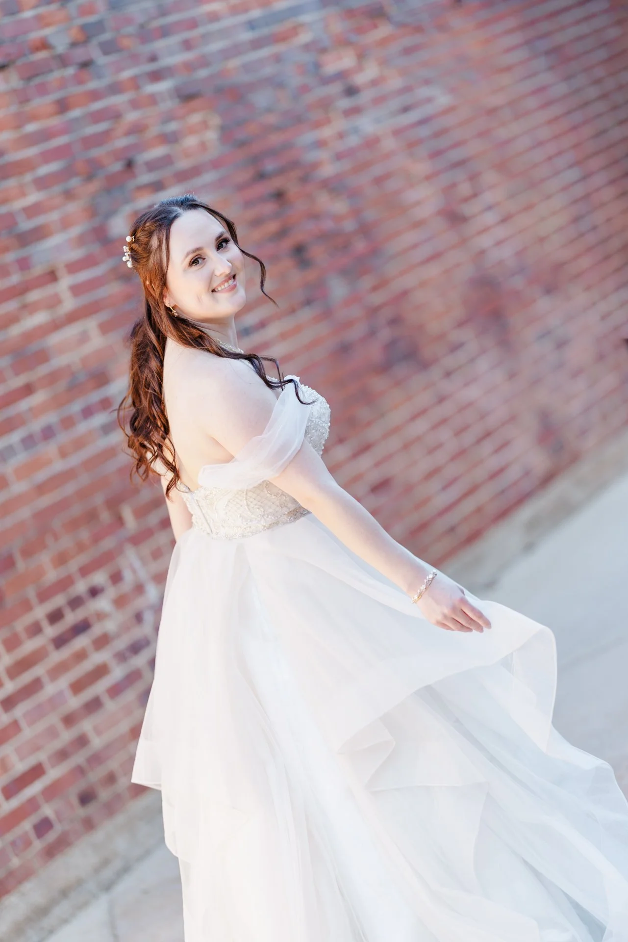 Bride looking back over her shoulder as the wind blows her hair and she adjusts her dress outdoors in the courtyard at The Long Room in Plaza Midwood light and airy photographed by Charlotte wedding photographer Michael Parks, ParksPictures film