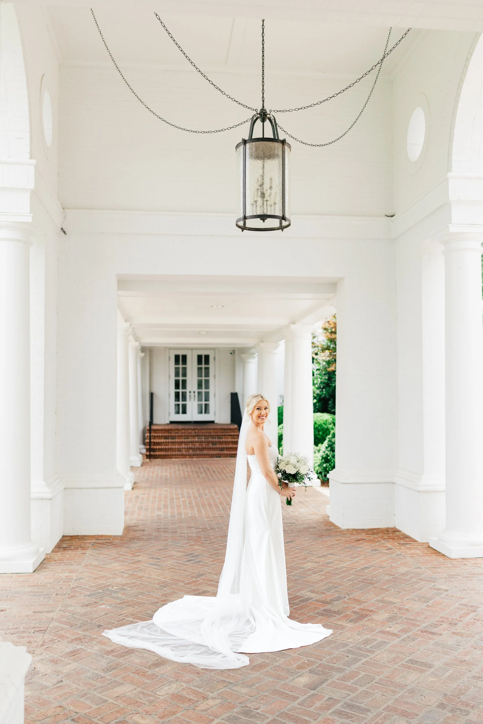 Bride looking over her shoulder in the walkway to the clubhouse with white pillars at her wedding at Quail Hollow Club PGA in Charlotte NC by wedding photographer Michael Parks, ParksPictures