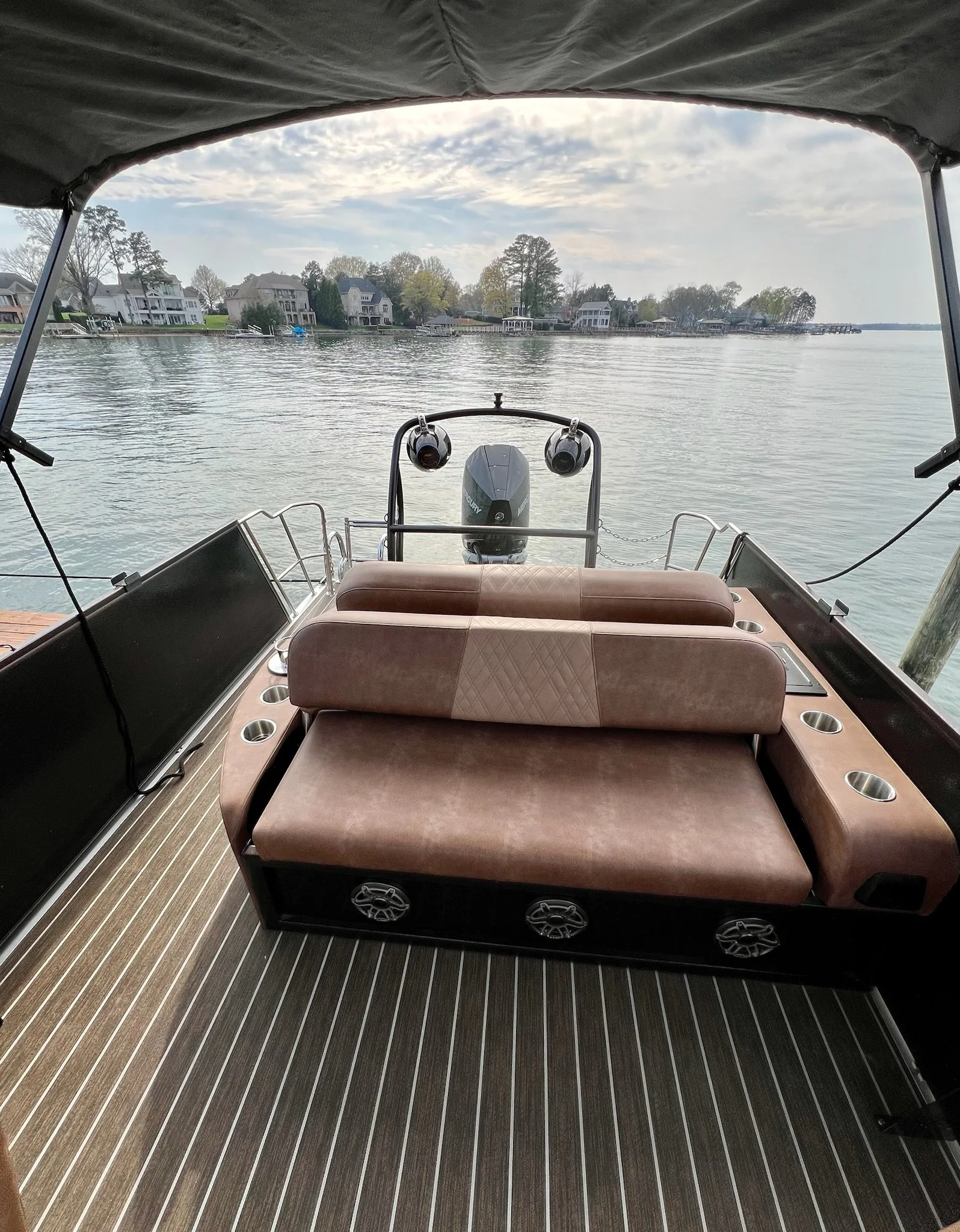 View of a boat with brown cushioned seating facing water with houses and trees in the background