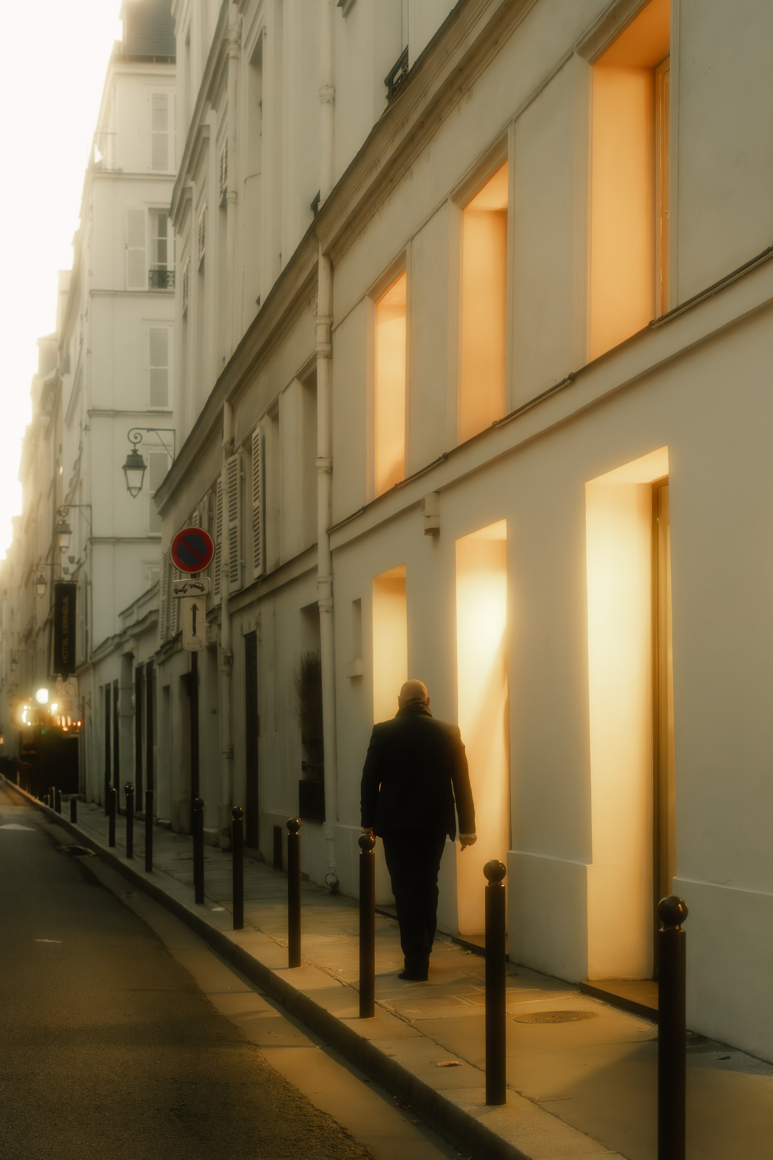 A person walking down a street at sunset with illuminated windows and white buildings.