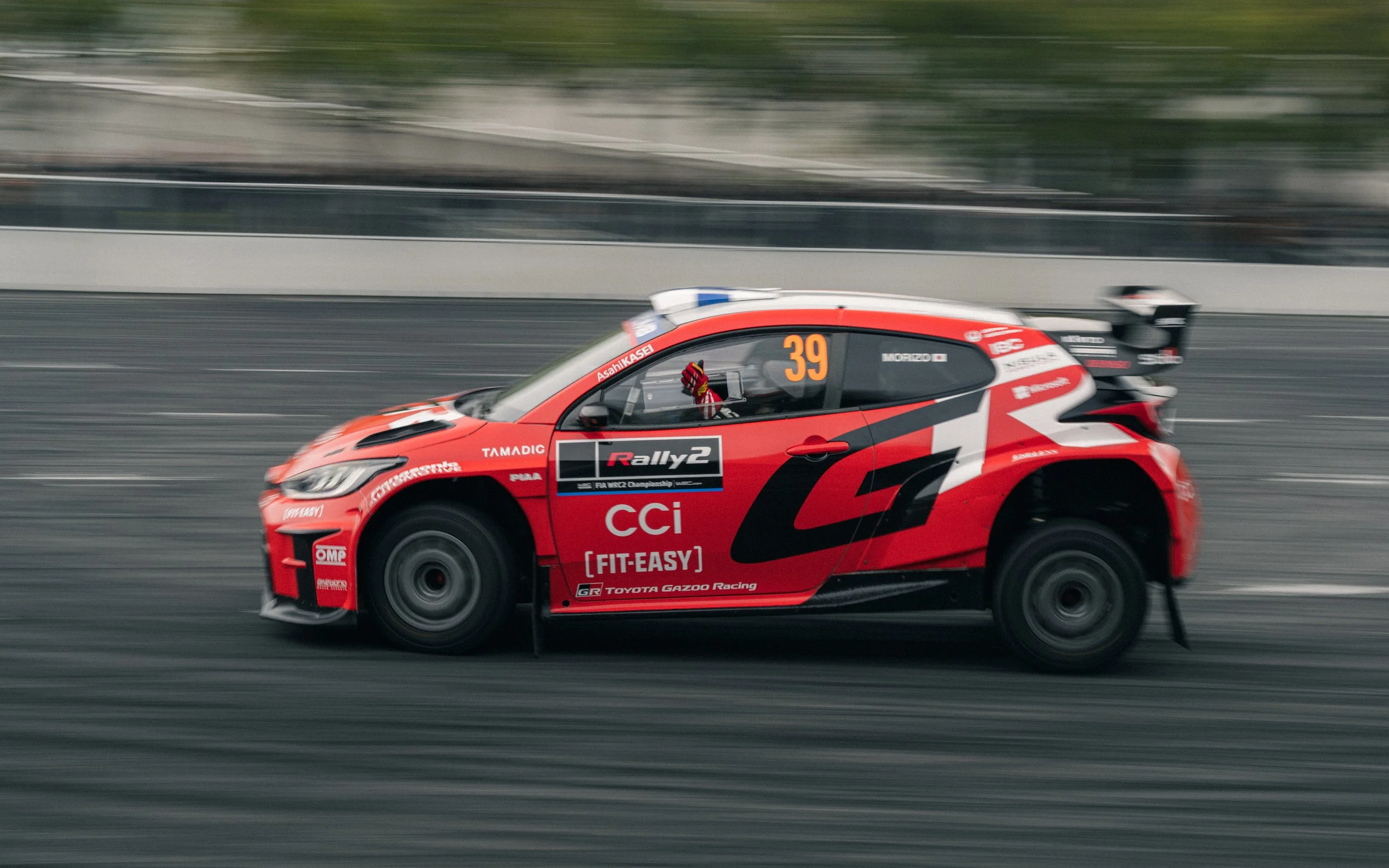 A red and black rally car racing on a track with motion blur.