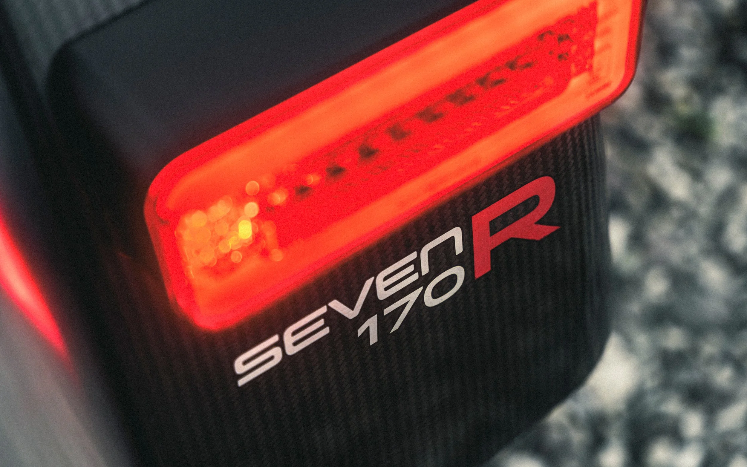 Close-up of an illuminated red taillight with the text 'SEVEN 170R' on its black surface.