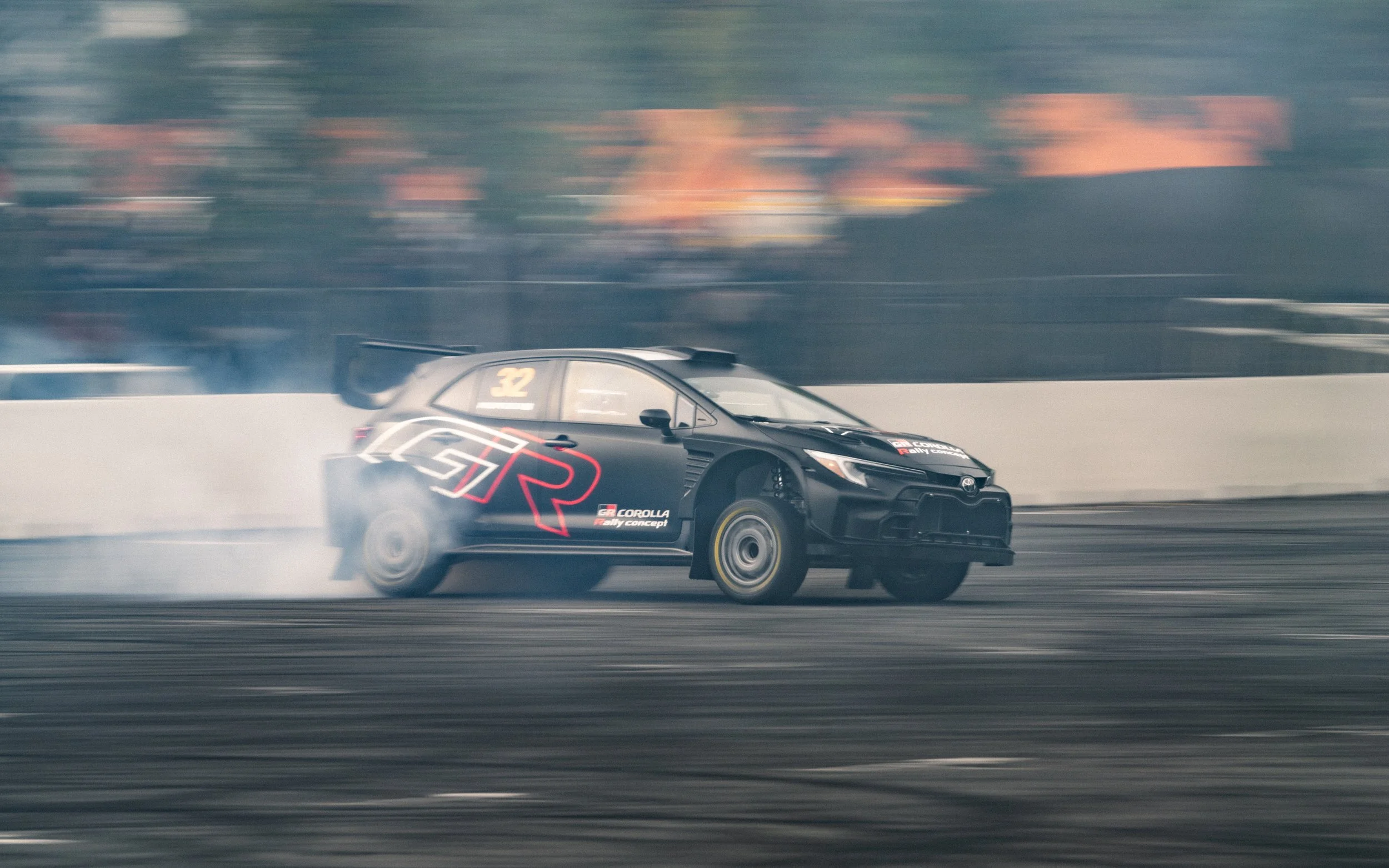 A black race car with the number 32 on the window, drifting and producing tire smoke on a racetrack.