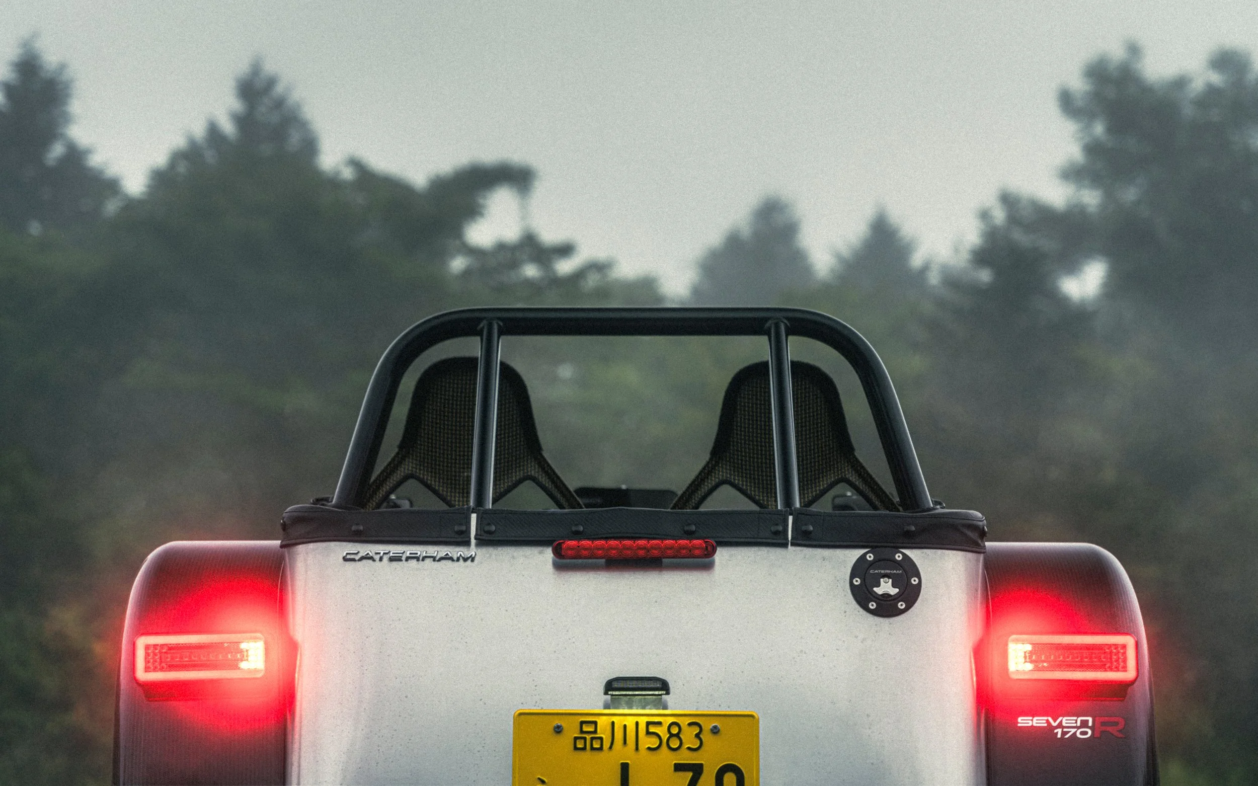 Rear view of a white Caterham Seven 170 R sports car, parked outdoors with brake lights on, showing seats and license plate.