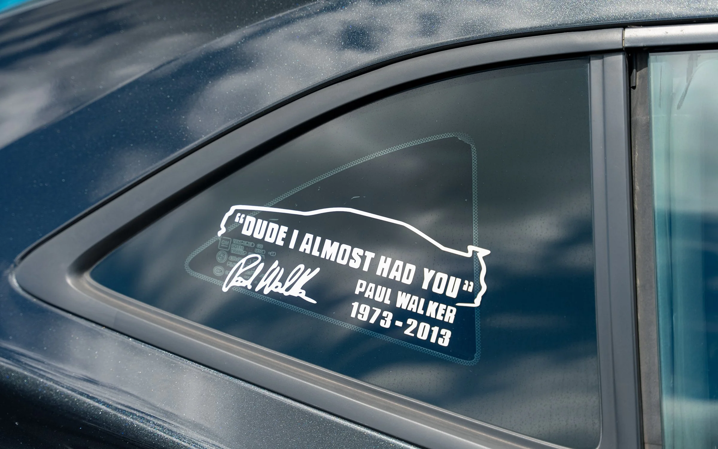 Car window with a decal quote that says, 'Dude I almost had you' by Paul Walker, with his signature and the years 1973-2013, in memory of Paul Walker.