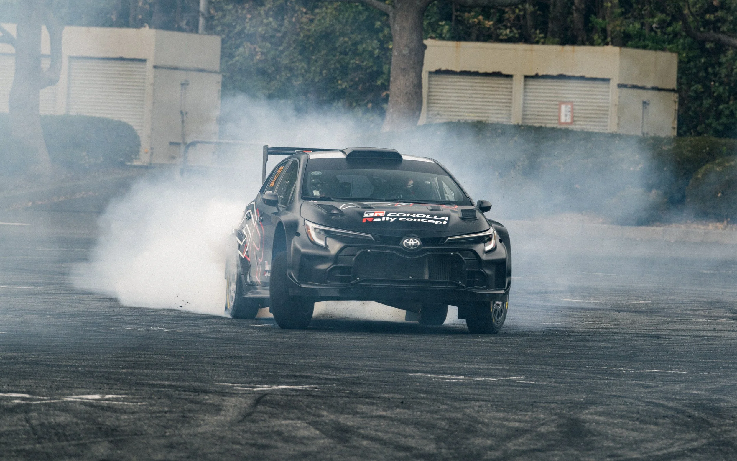 A black Toyota rally car drifting around a corner on a dirt track, creating a cloud of dust.