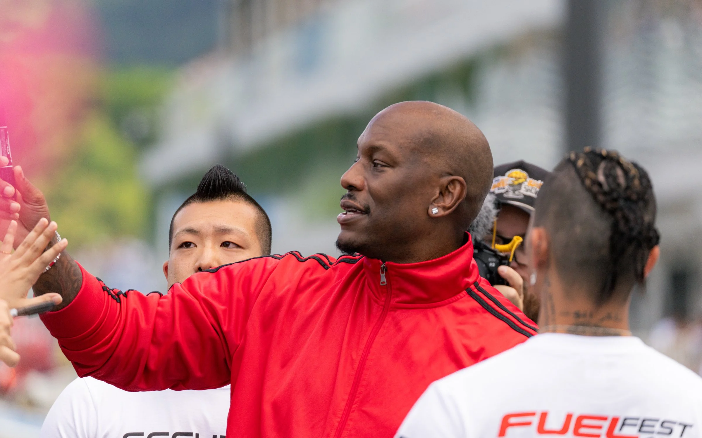 A man in a red sports jacket taking a selfie with a group of people.