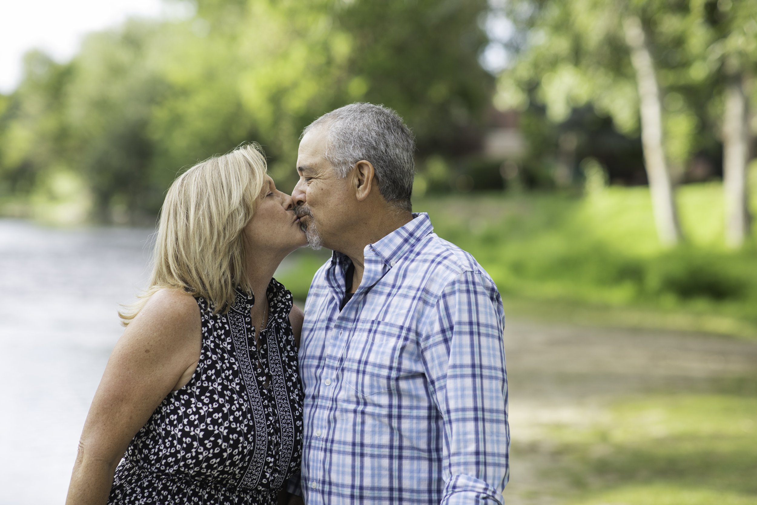 A middle-aged couple sharing a kiss outdoors in a lush park.