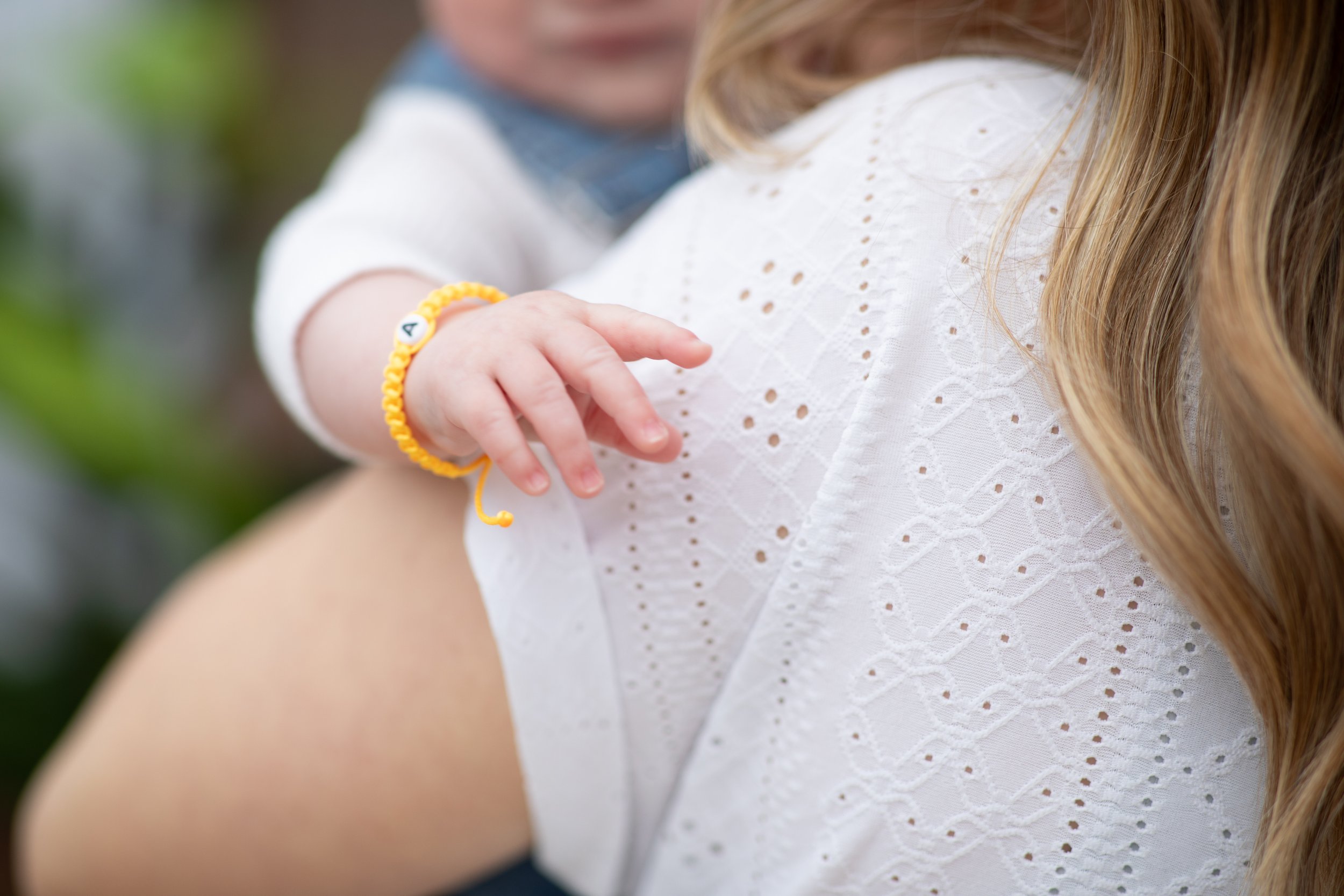 A young child with a yellow bracelet on their wrist, reaching out and touching a woman with long, light brown hair wearing a white embroidered top.