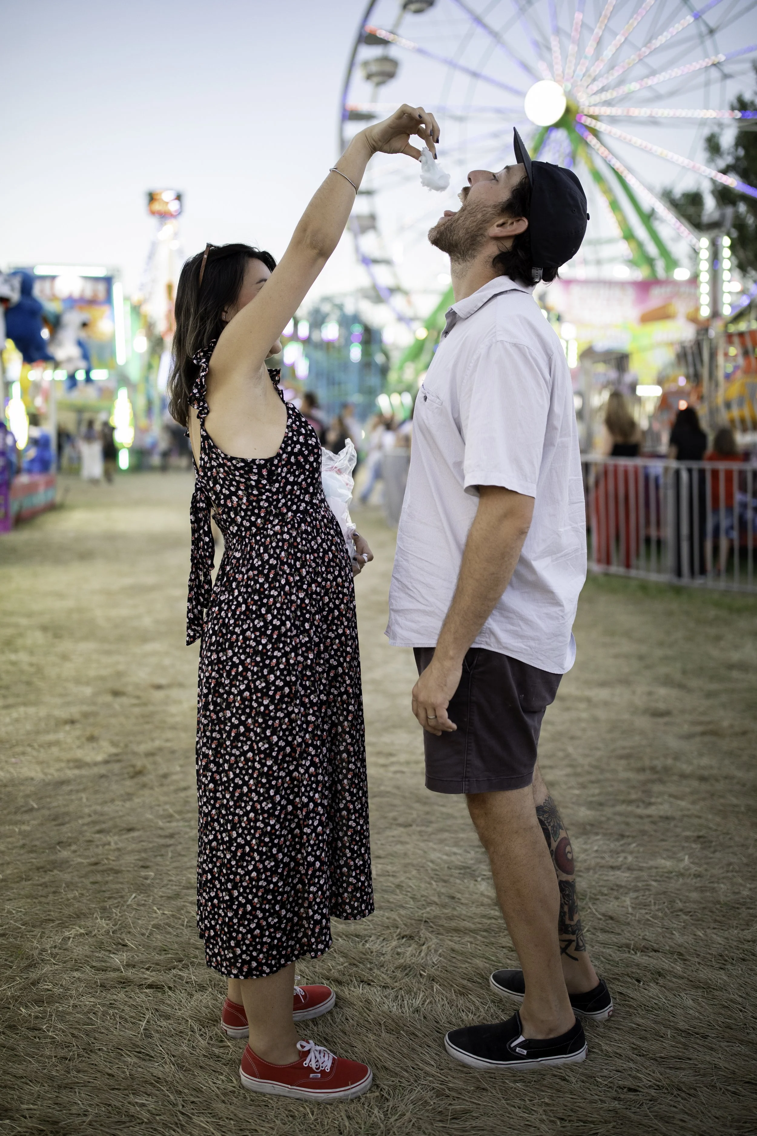 A woman and a man at a fairground, where the woman is feeding a cotton candy to the man.