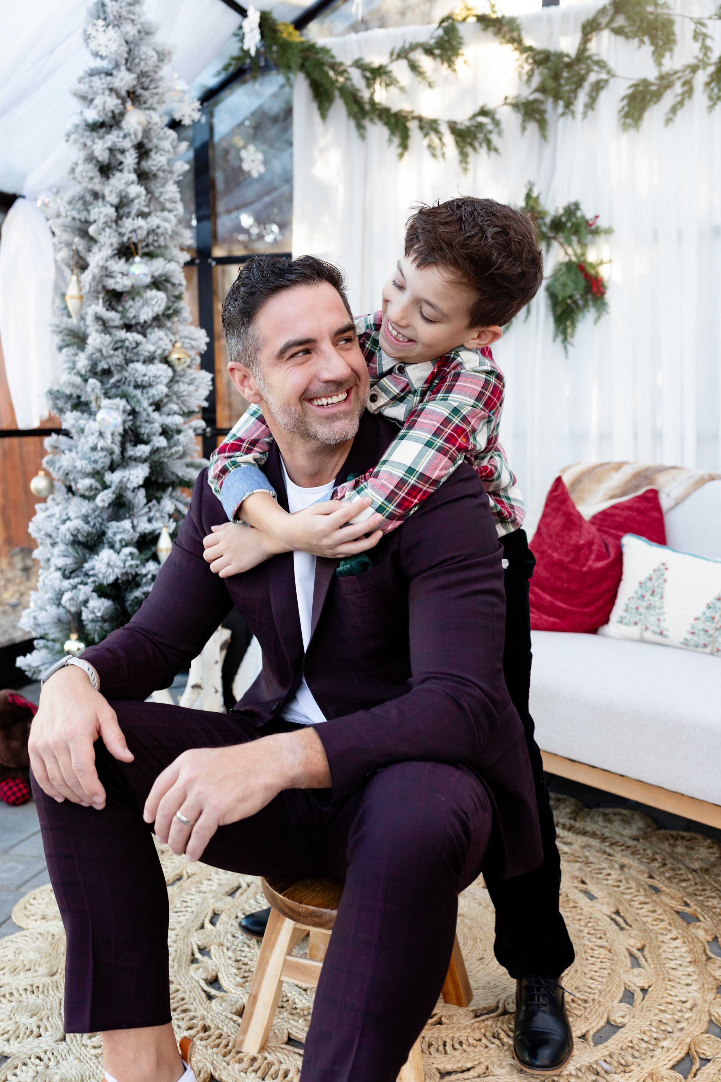 A man and a boy enjoying time together in a holiday decorated room, with a Christmas tree and festive decorations visible in the background.