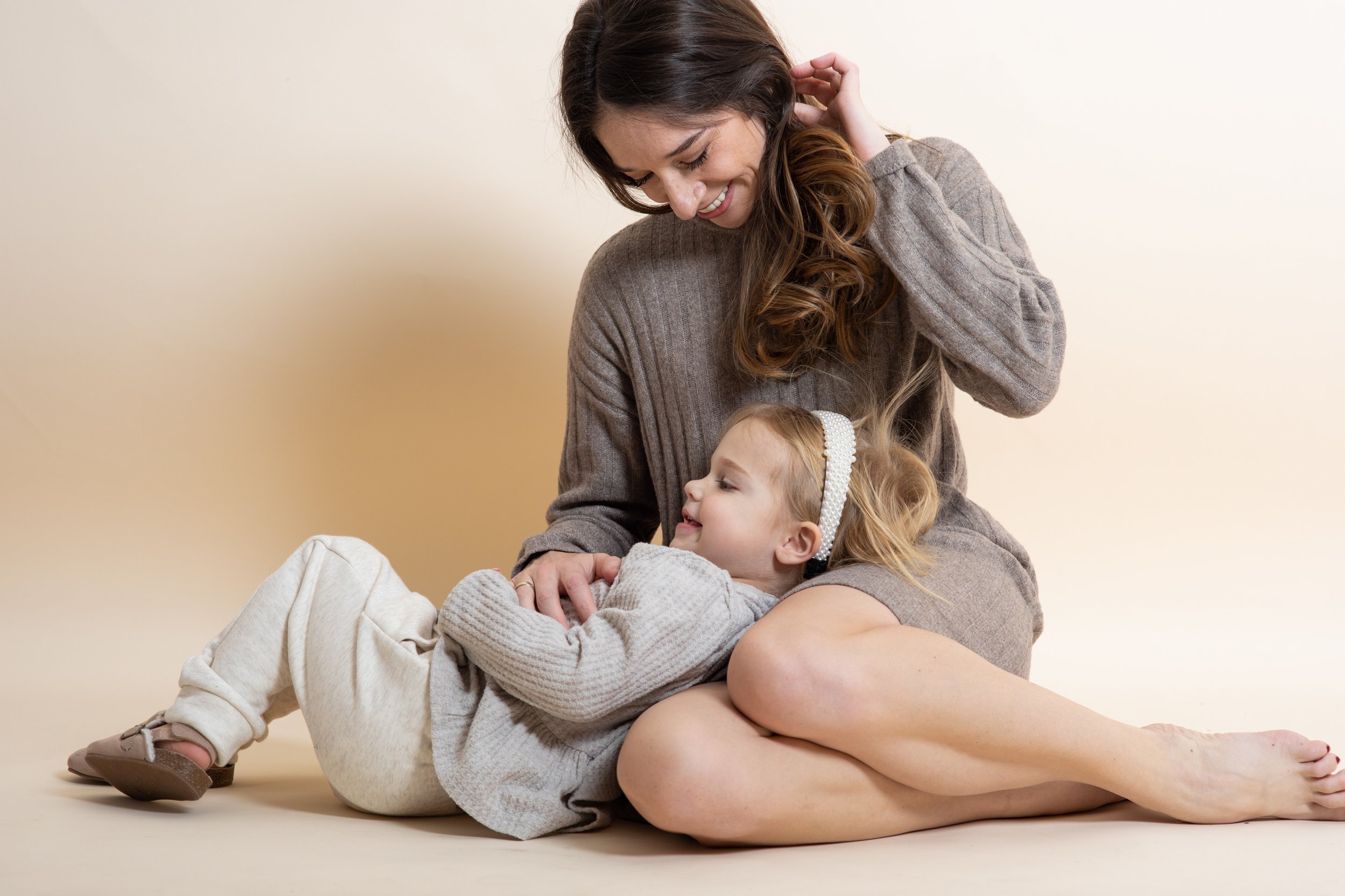 A woman and a young girl sitting on the floor, smiling and looking at each other, in a warm and intimate moment.