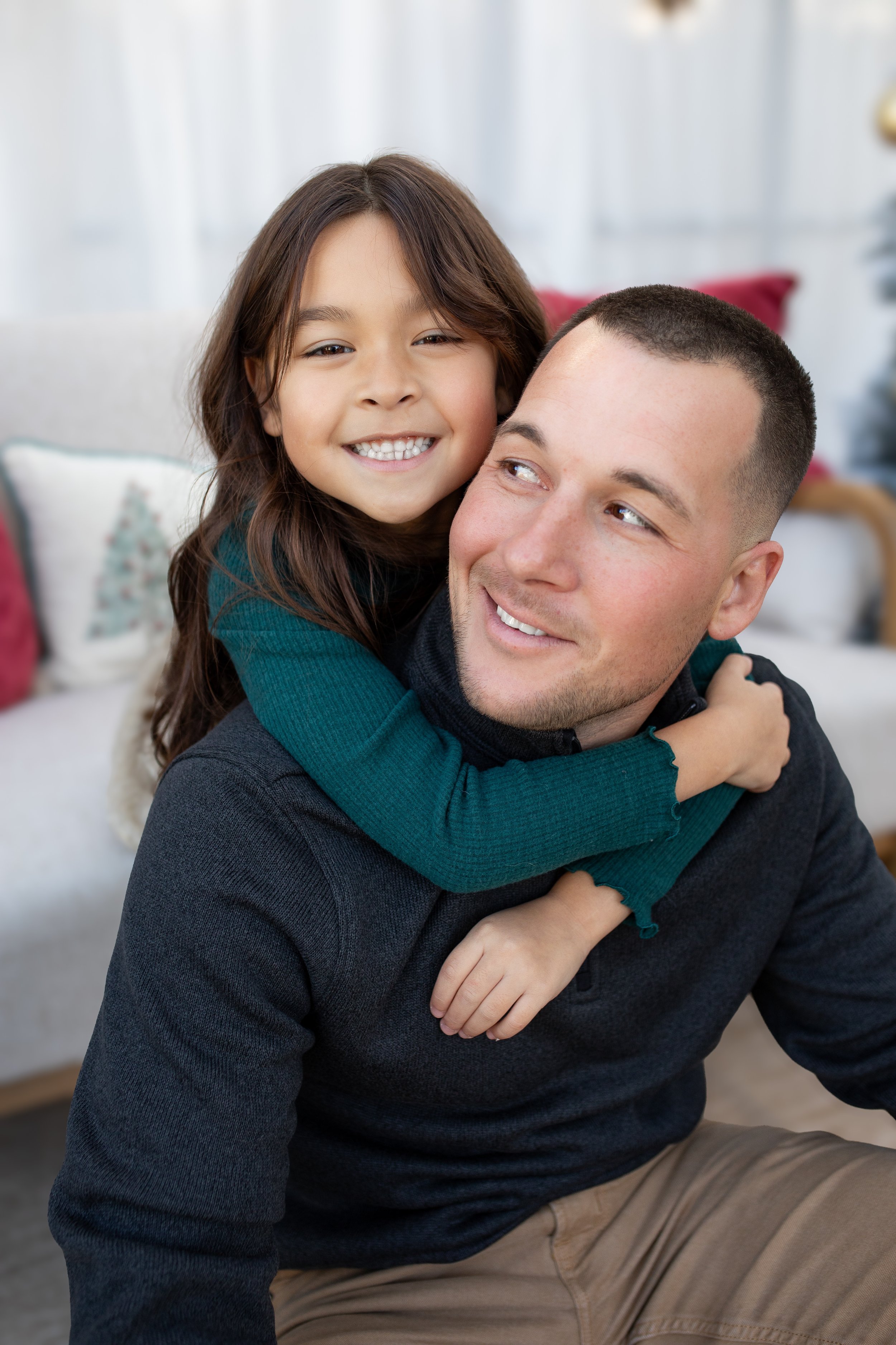 A young girl hugging her father from behind, both smiling warmly.