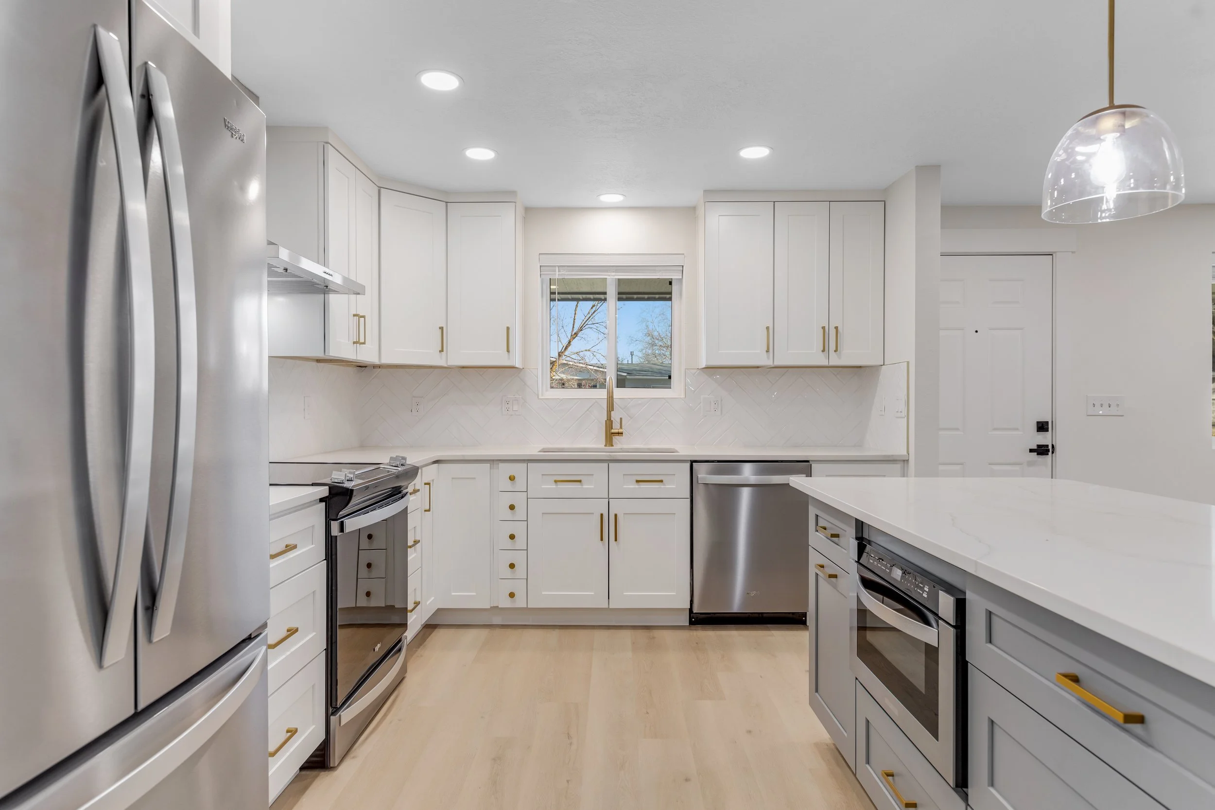Modern kitchen with white cabinets, gold handles, stainless steel appliances, a central island, and a window above the sink.