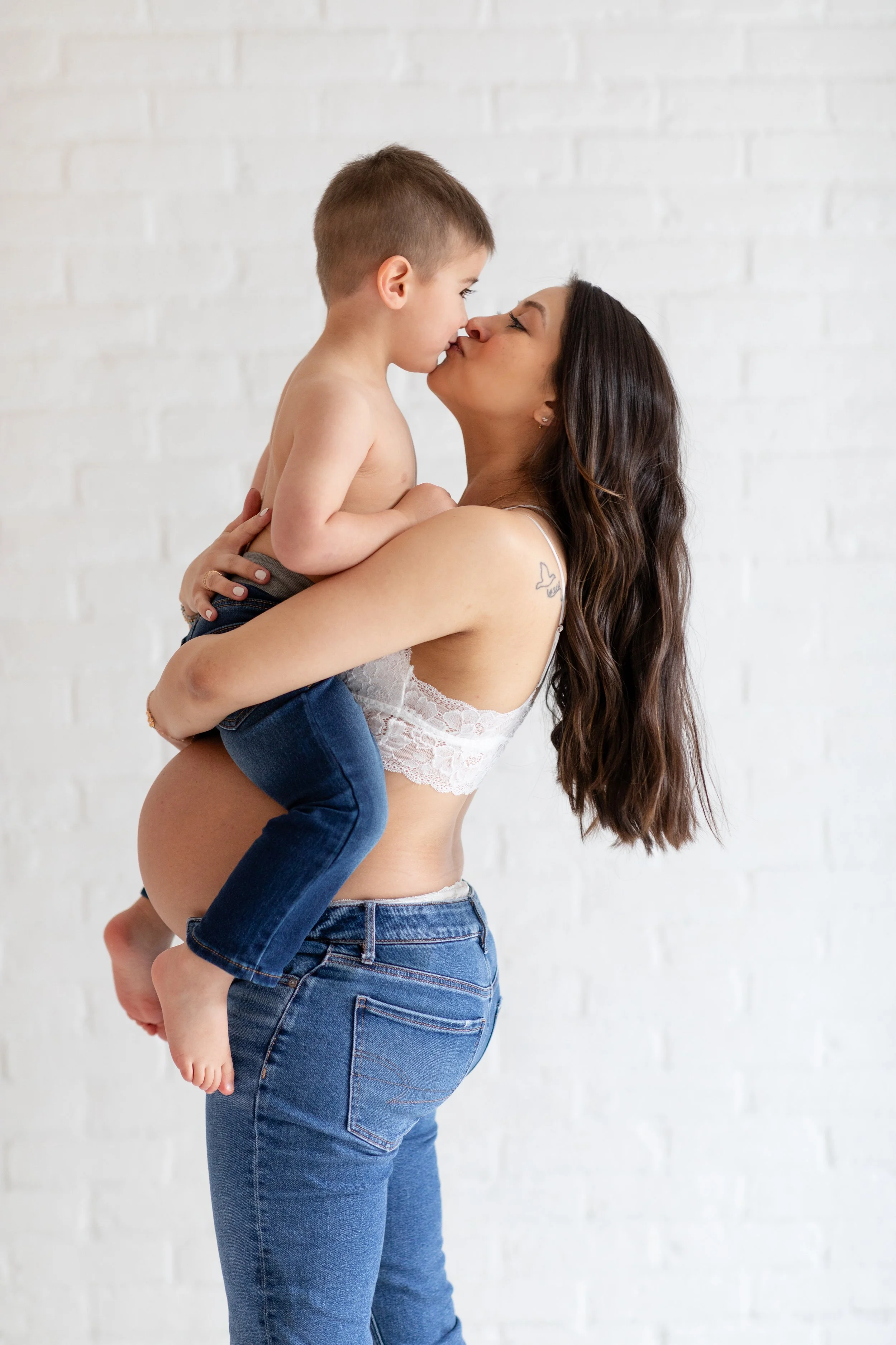 A woman holding a young boy, touching noses, against a white brick wall.