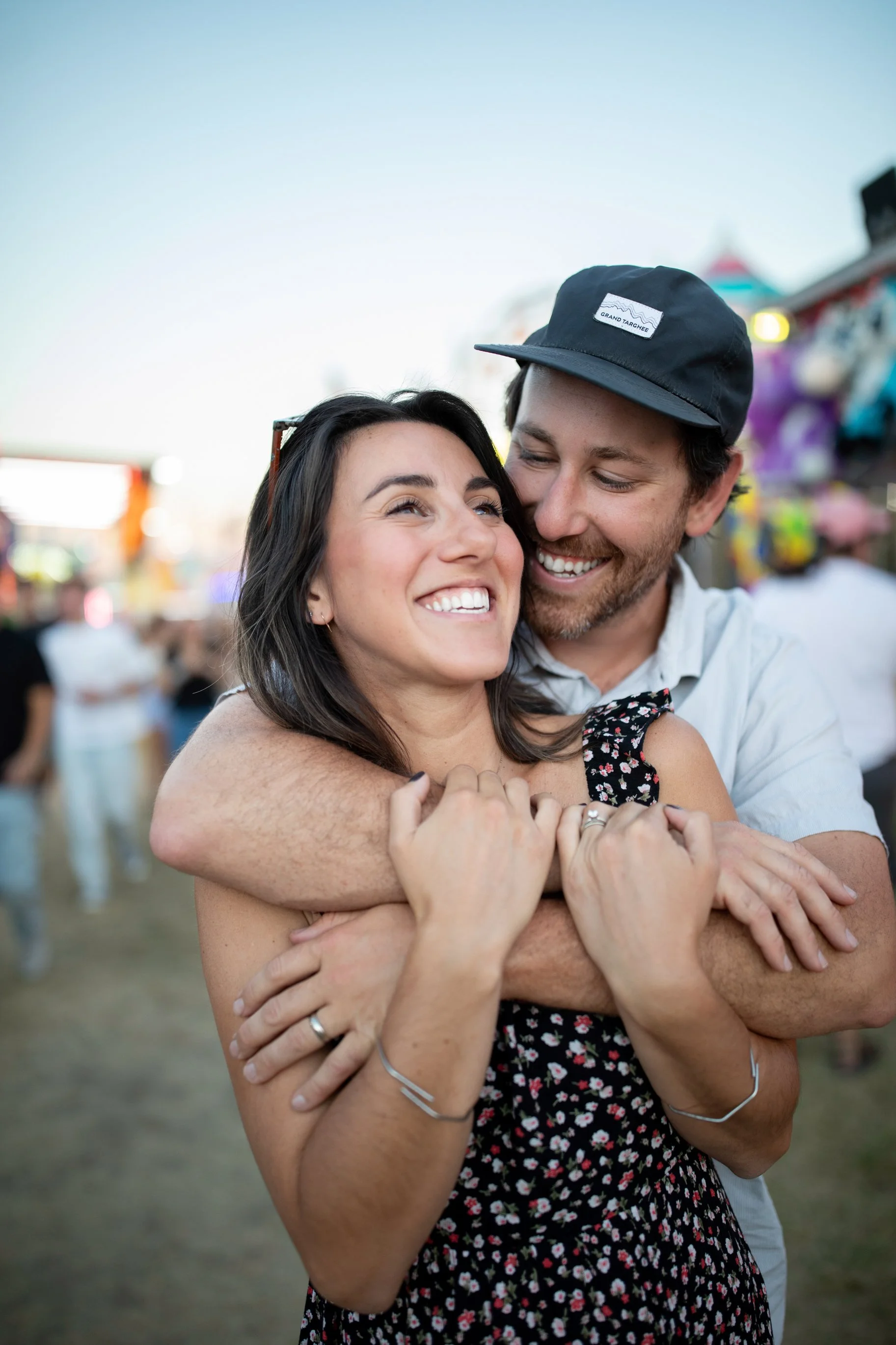 A couple embracing and smiling at each other at an outdoor fair or festival.