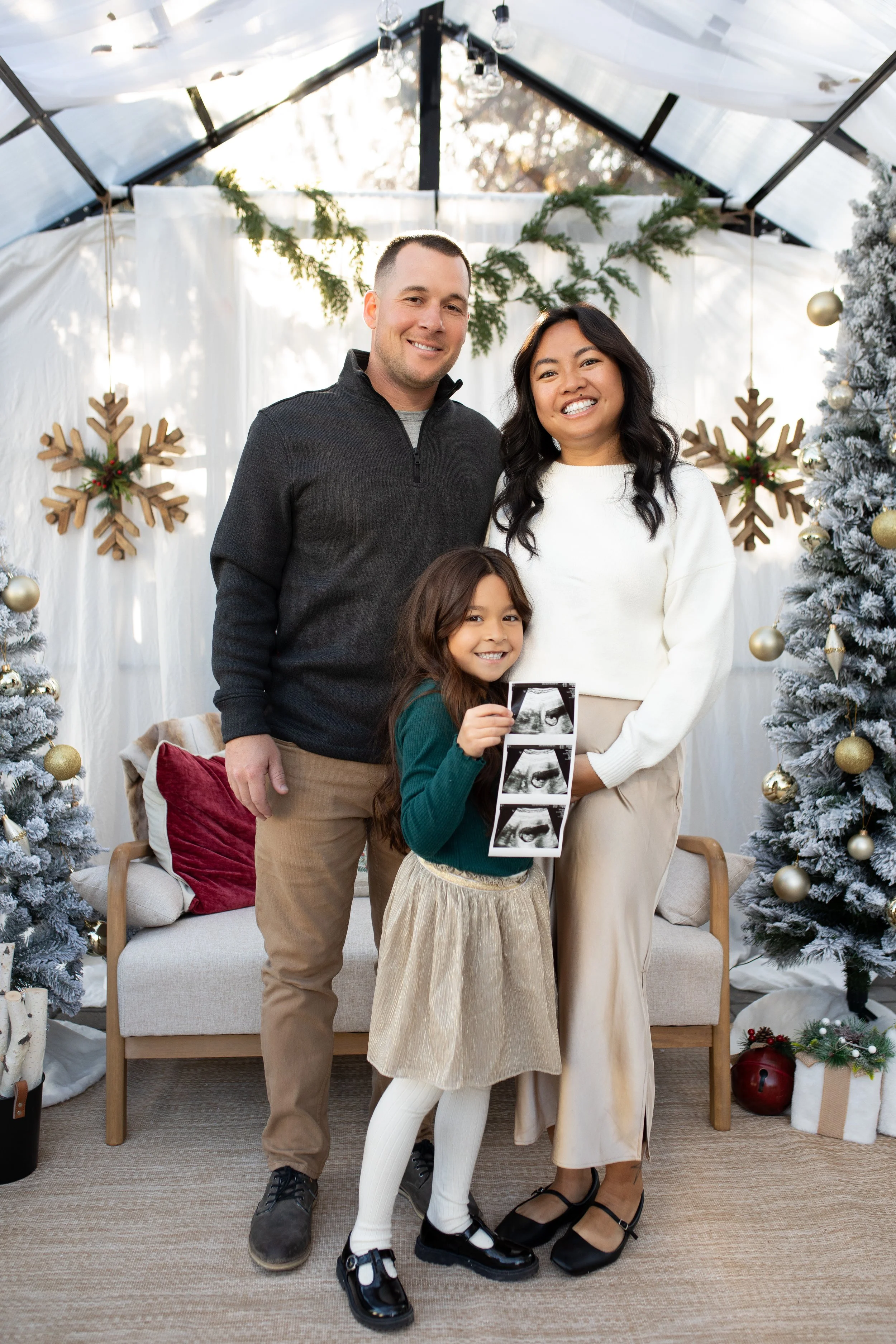 Family of four celebrating Christmas with festive decorations, Christmas trees, and snowflakes, holding ultrasound images.
