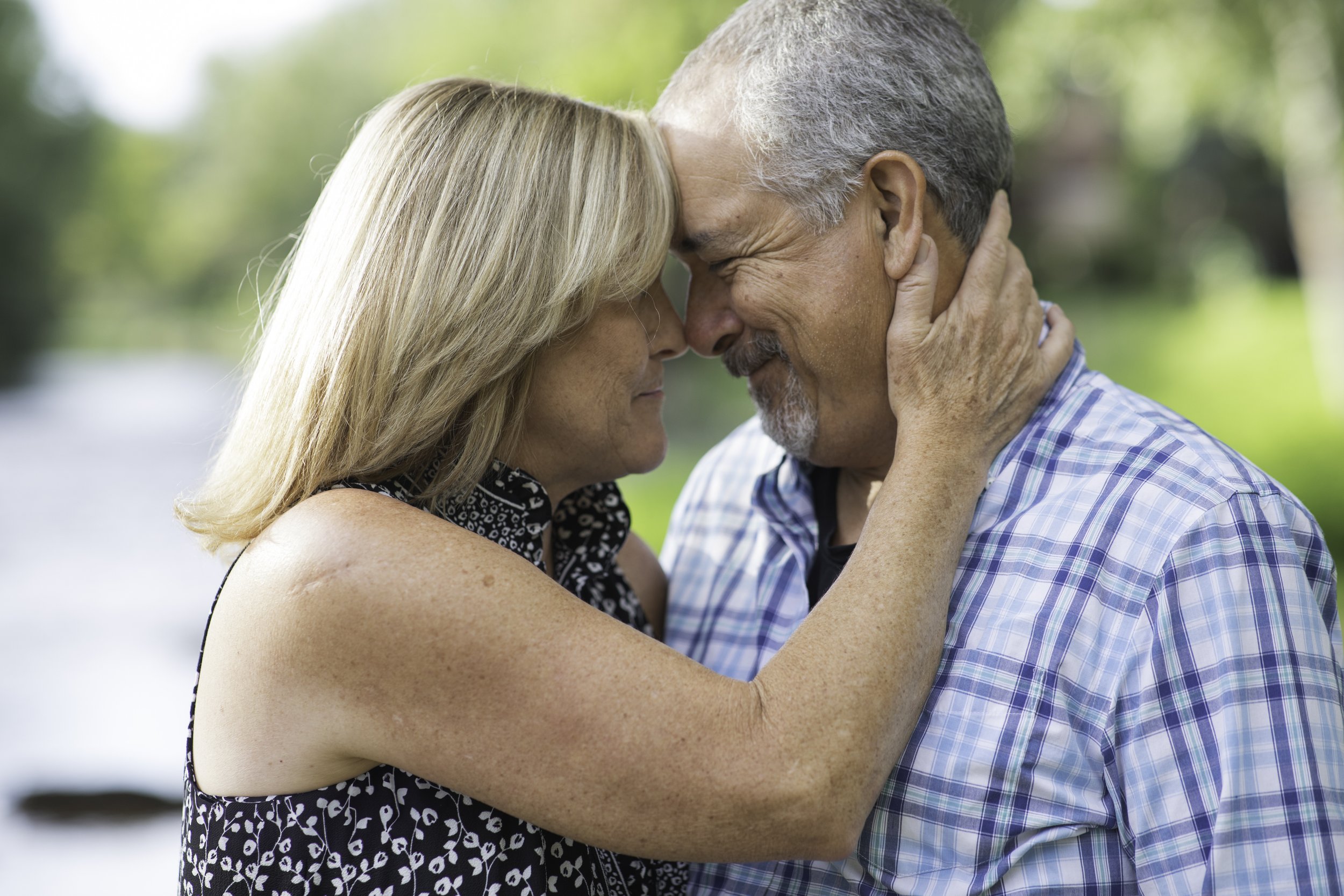 Older couple touching foreheads and smiling outdoors on a sunny day.