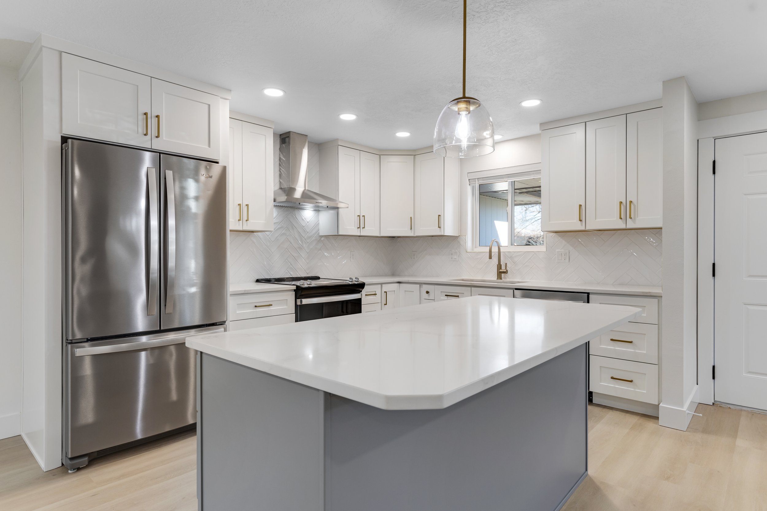 Modern kitchen with white cabinets, stainless steel refrigerator, black stove, and white countertop island.