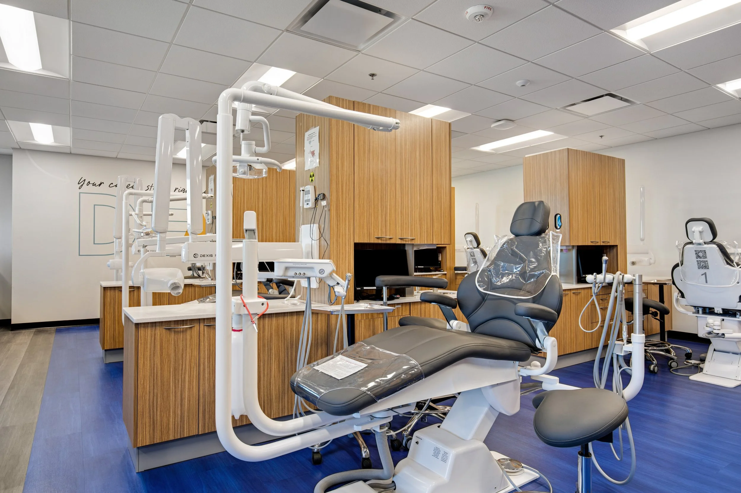 A dental clinic room with dental chairs and equipment, wooden cabinets, and a modern, clean design.