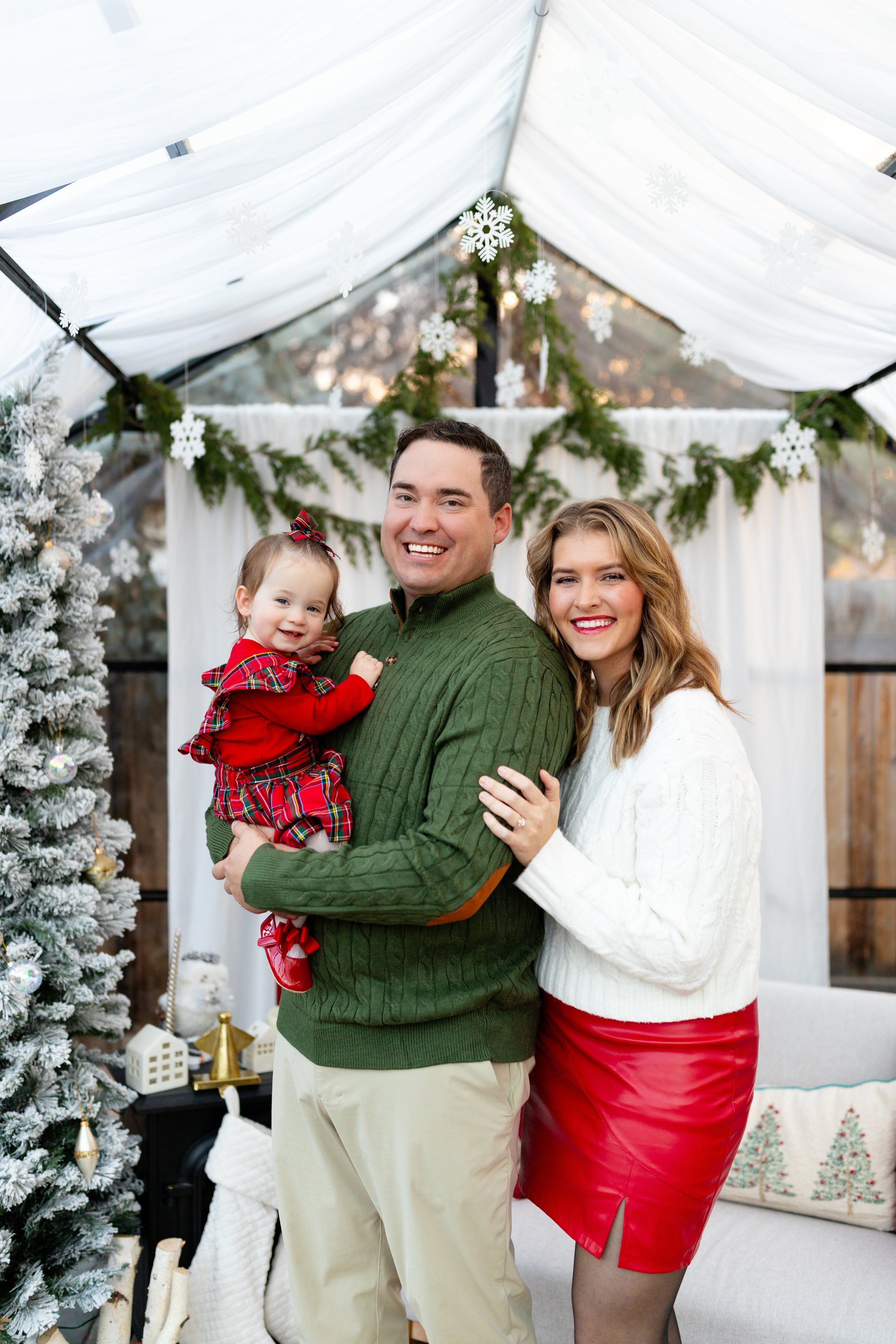 A family of three celebrating Christmas indoors, with a decorated Christmas tree, wrapped presents, and festive decorations.