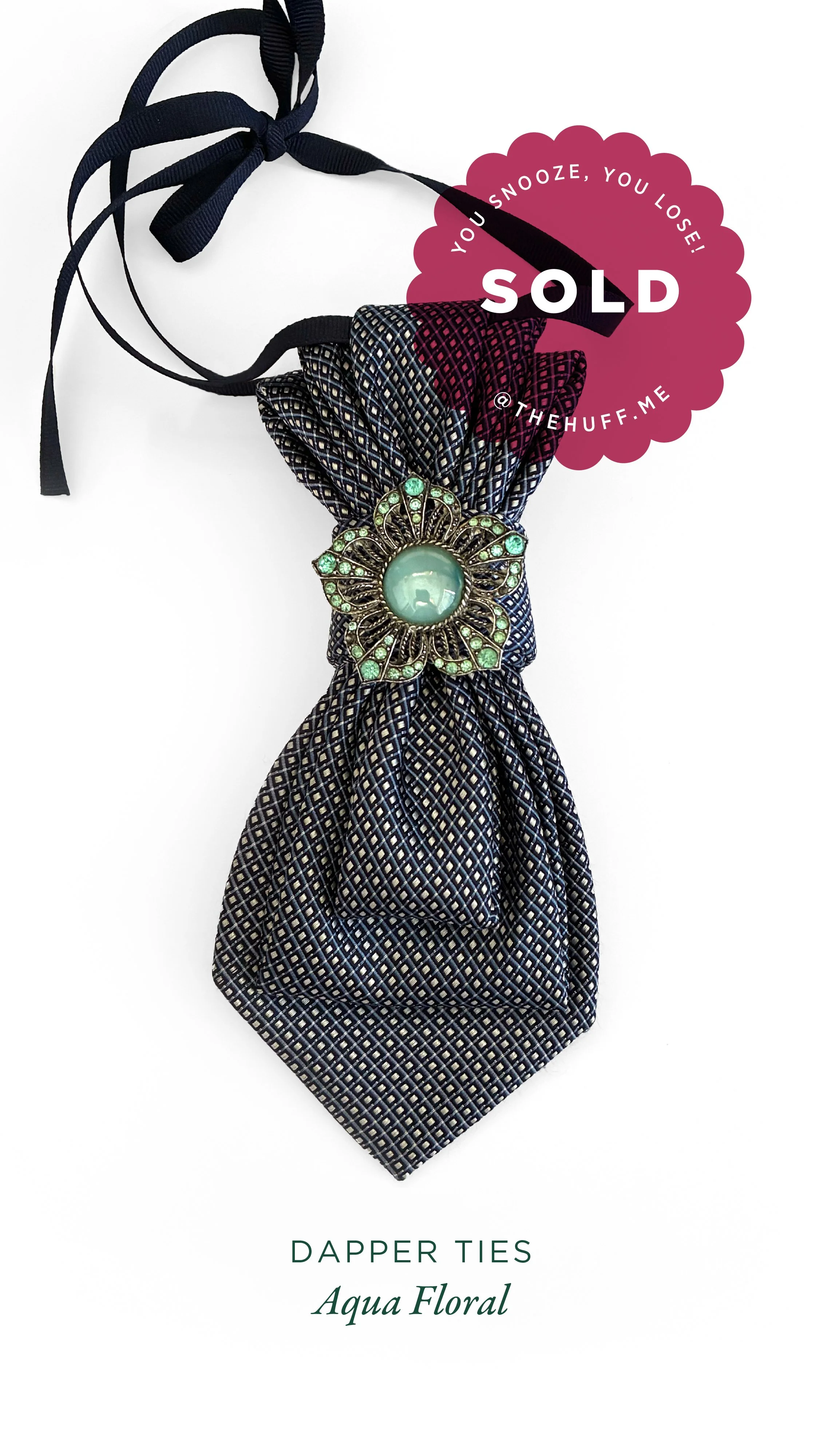 A navy blue patterned tie with a floral brooch and neck ribbon, labeled as sold.
