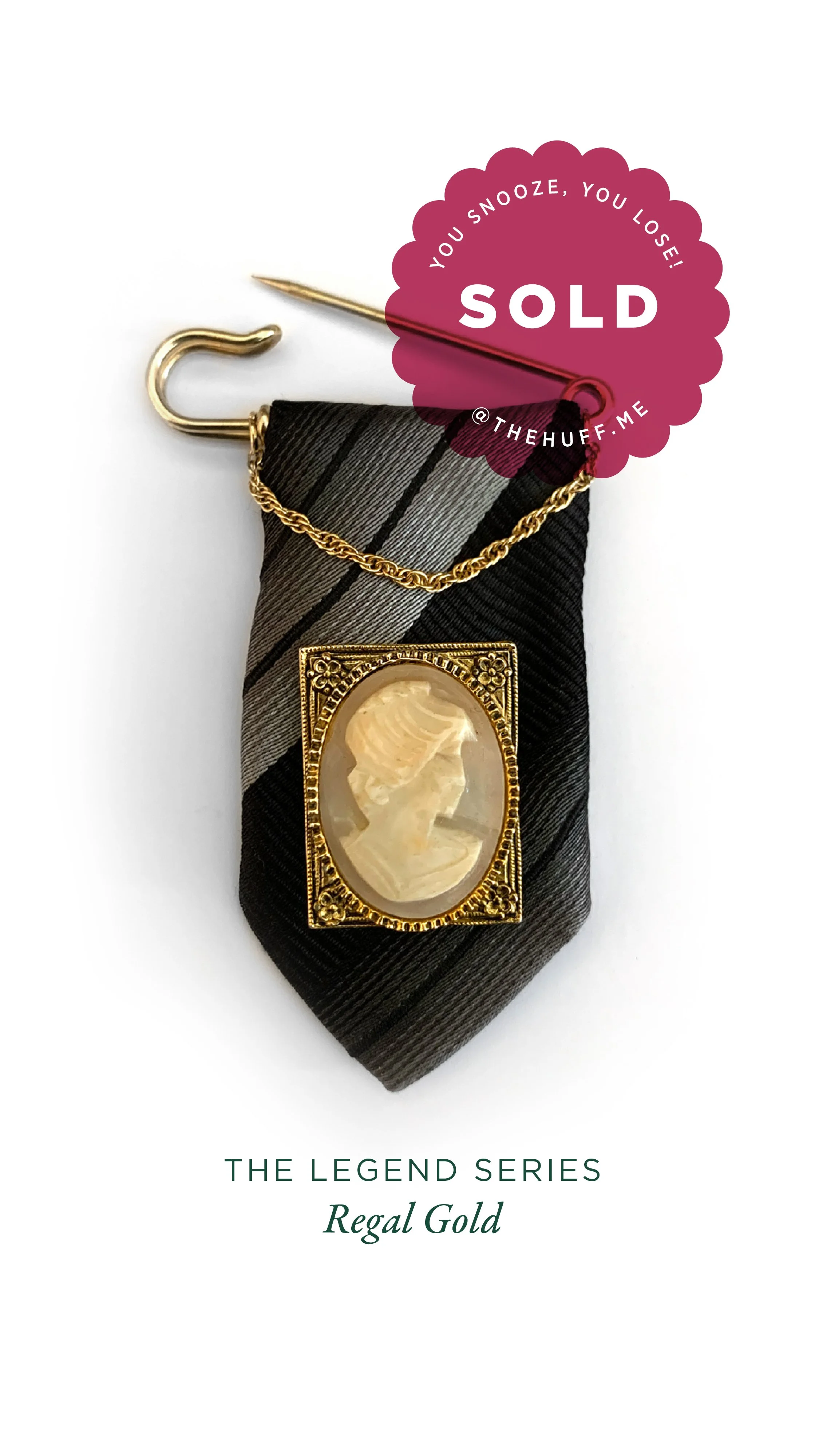 A decorative cameo brooch with a gold frame, attached to a black and gray striped fabric tie, with a gold chain and a pin, against a white background, marked as sold.