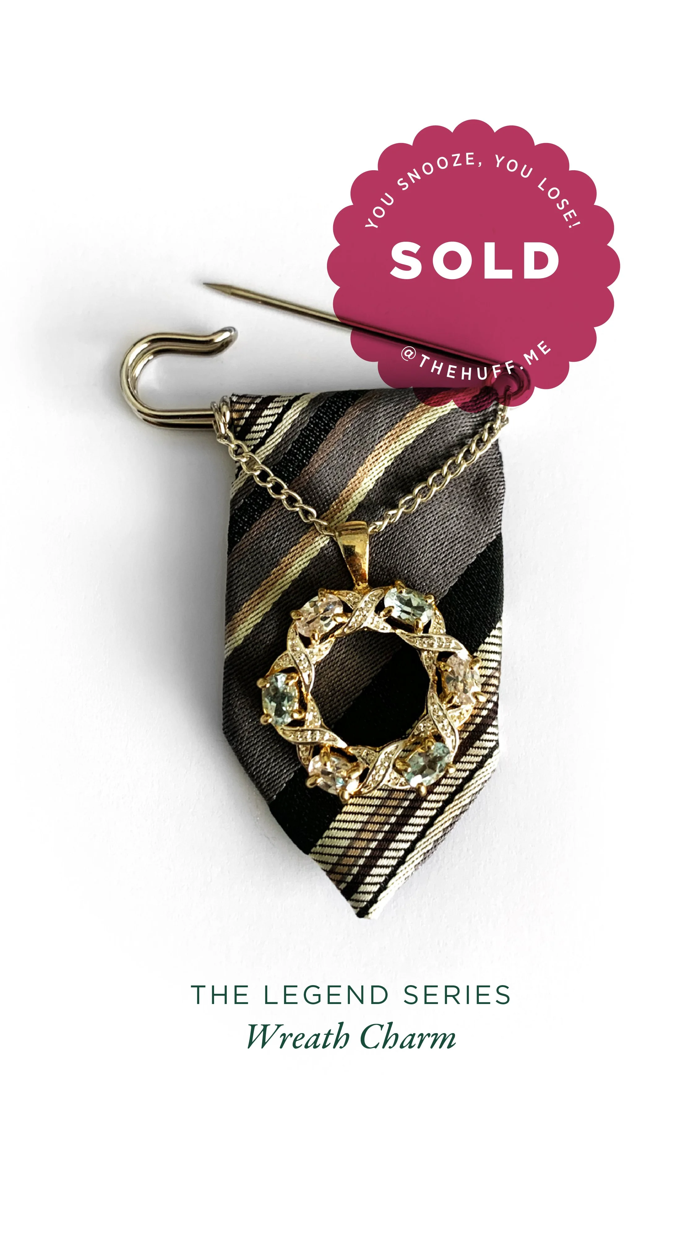 A decorative wreath-shaped charm with gemstones, hanging on a striped fabric tie, attached to a safety pin, with a sold sticker on the top right