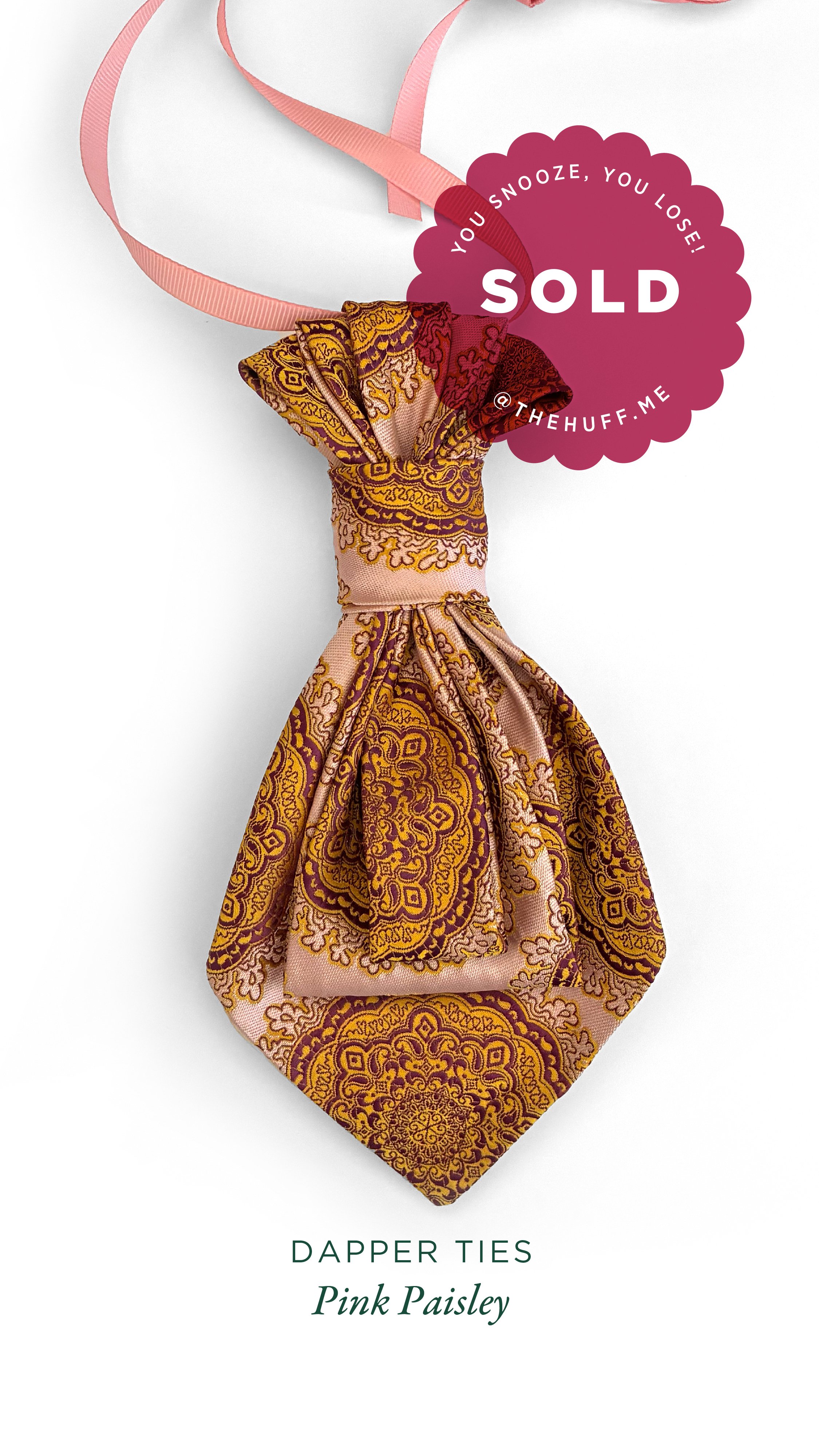 A pink paisley dapper tie, fastened with a pink ribbon, displayed against a white background with a sold sticker indicating it was bought.