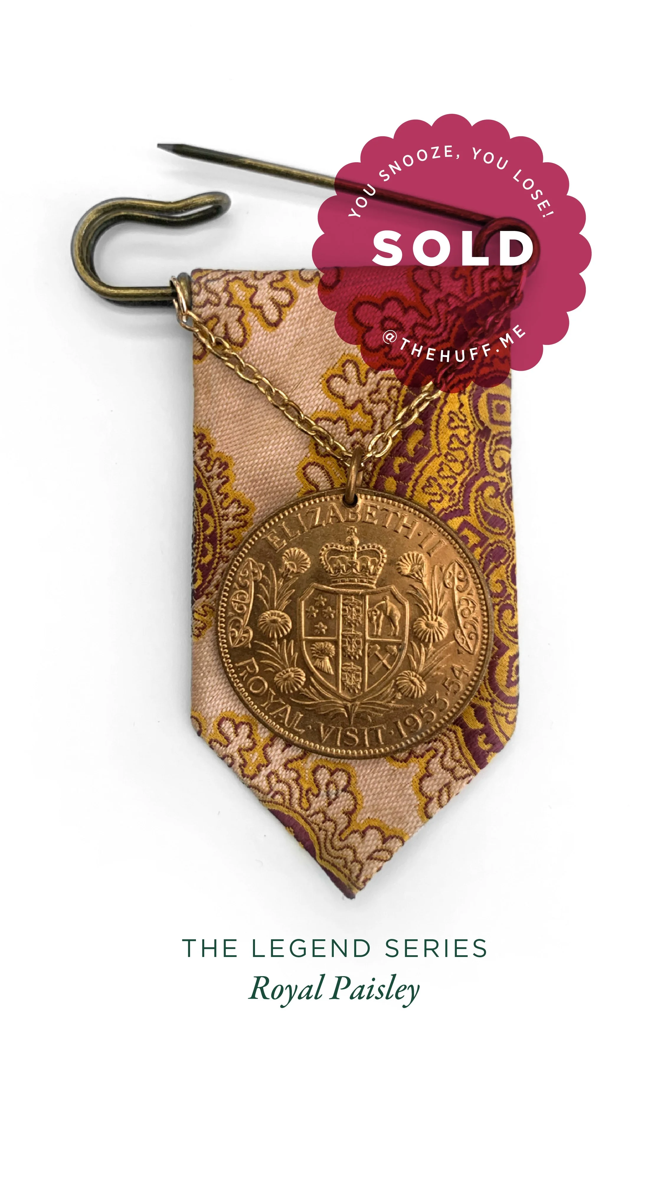 A pin with a pink and gold paisley ribbon, a gold chain with a large gold coin pendant, and a safety pin attached, with a sold sticker overlapping the top right corner. The coin features the portrait of Queen Elizabeth II, the crown, and inscriptions
