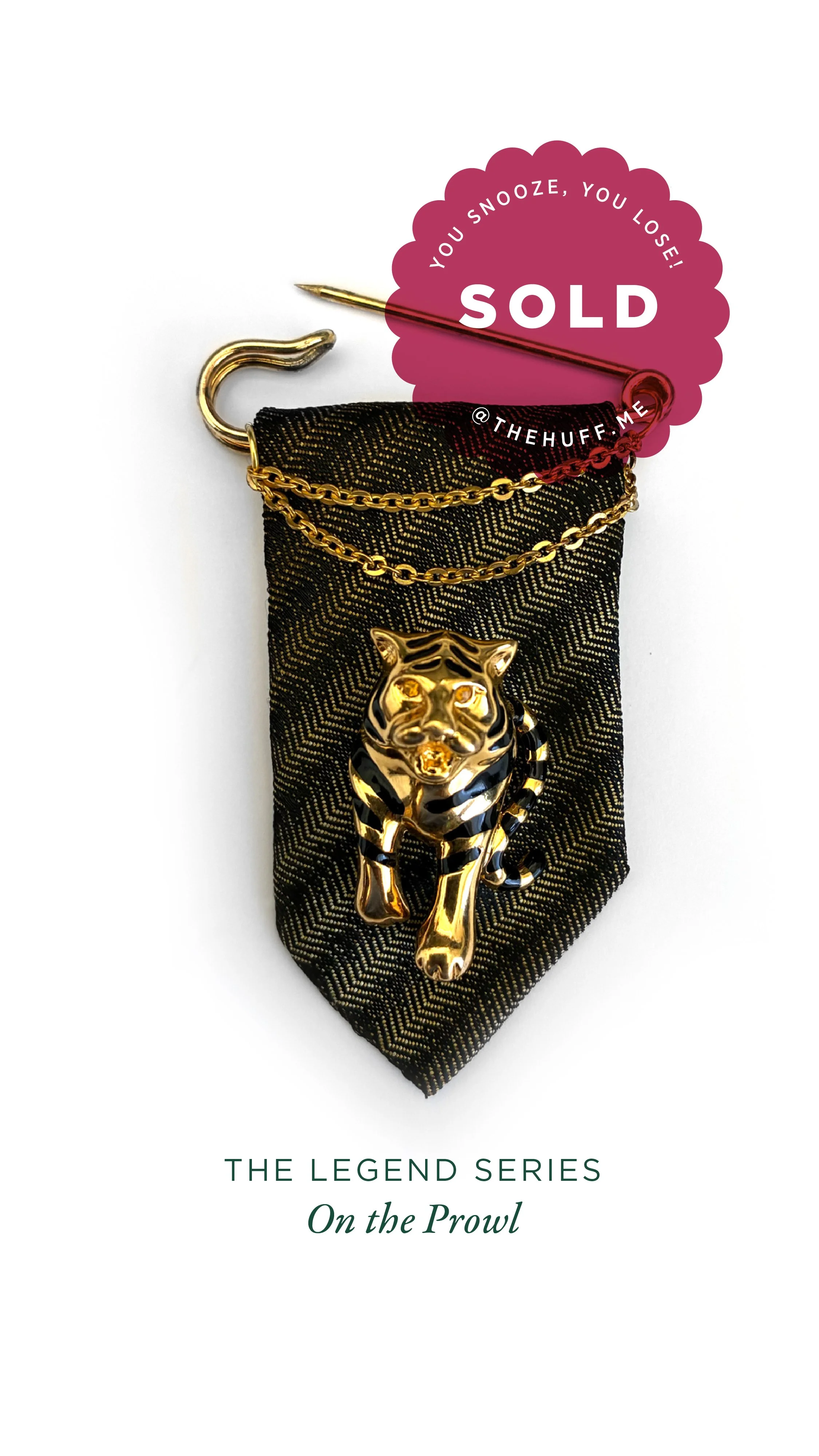 Black and gold brooch of a tiger, attached to black fabric with gold diagonal stripes, with a gold chain over it. Red circular sticker with 'SOLD' and a pin, with the text 'You snooze, you lose!' and '@thehuff.me'.