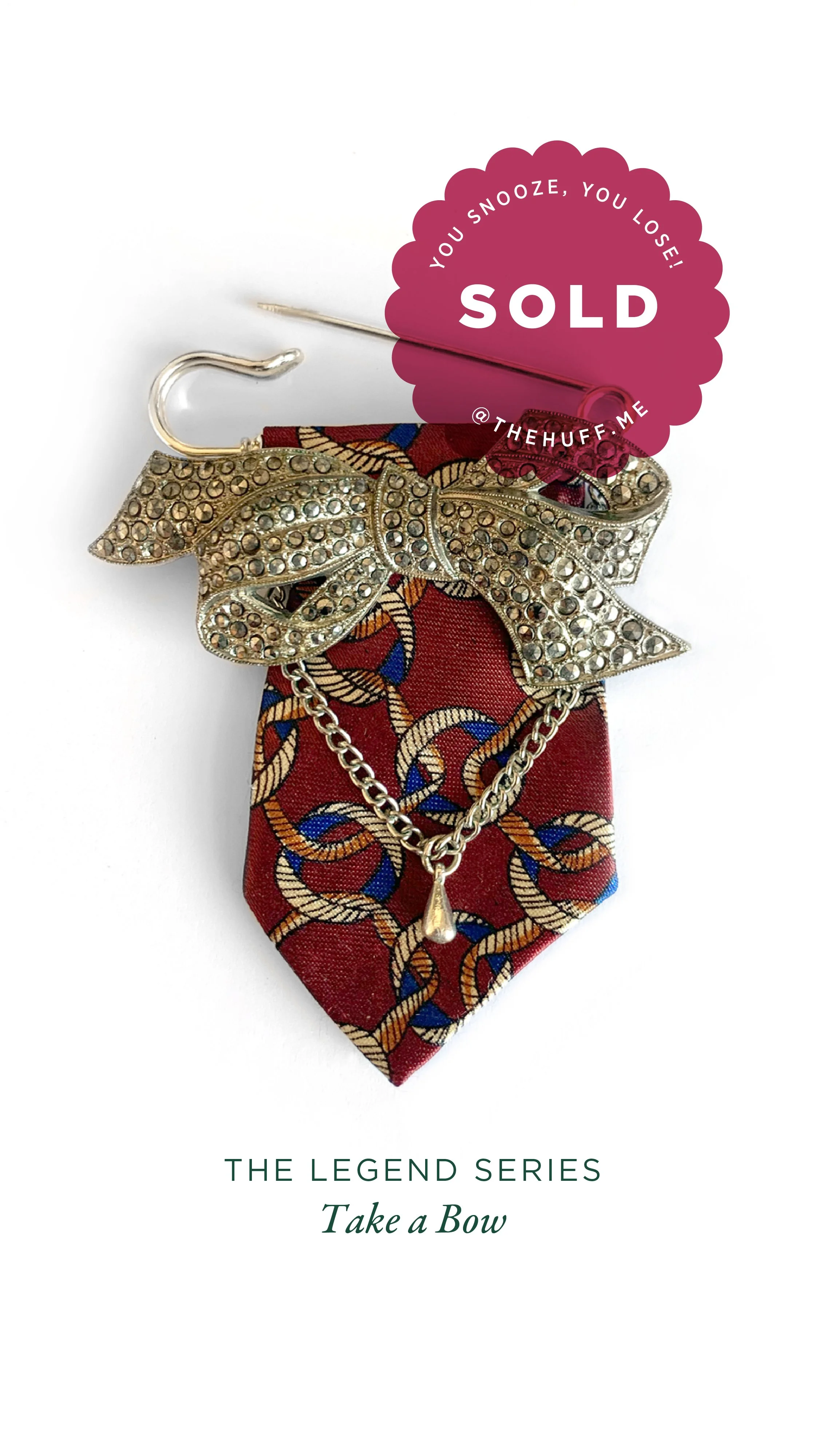 A decorative bow pin with rhinestones, attached to a burgundy toe blade with chain pattern, with a chain and teardrop pendant, labeled 'Take a Bow' on a white background.