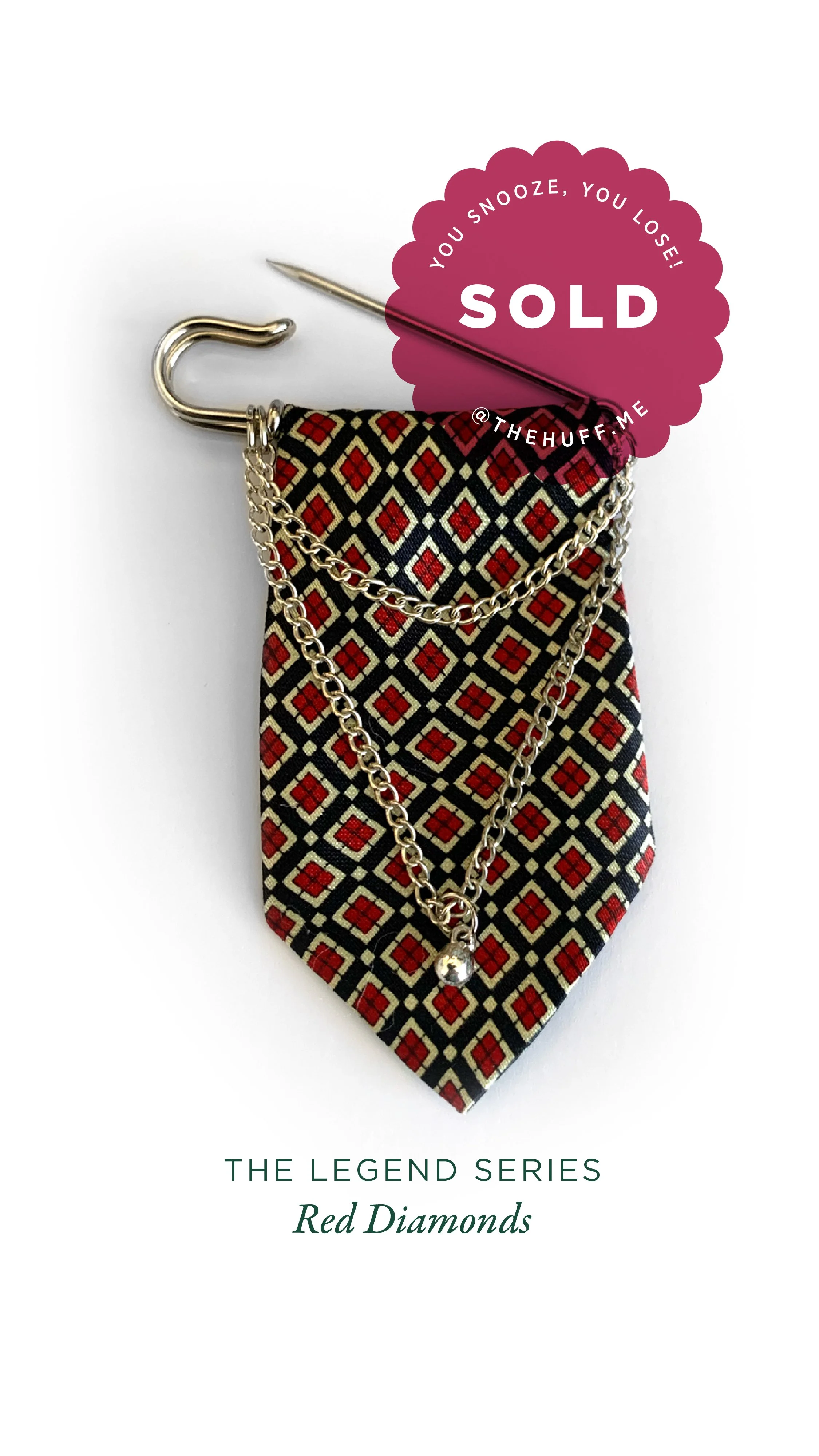 Red diamond patterned tie blade with layered silver chains, a pendant with a small silver charm, a pin with a purple "SOLD" label.